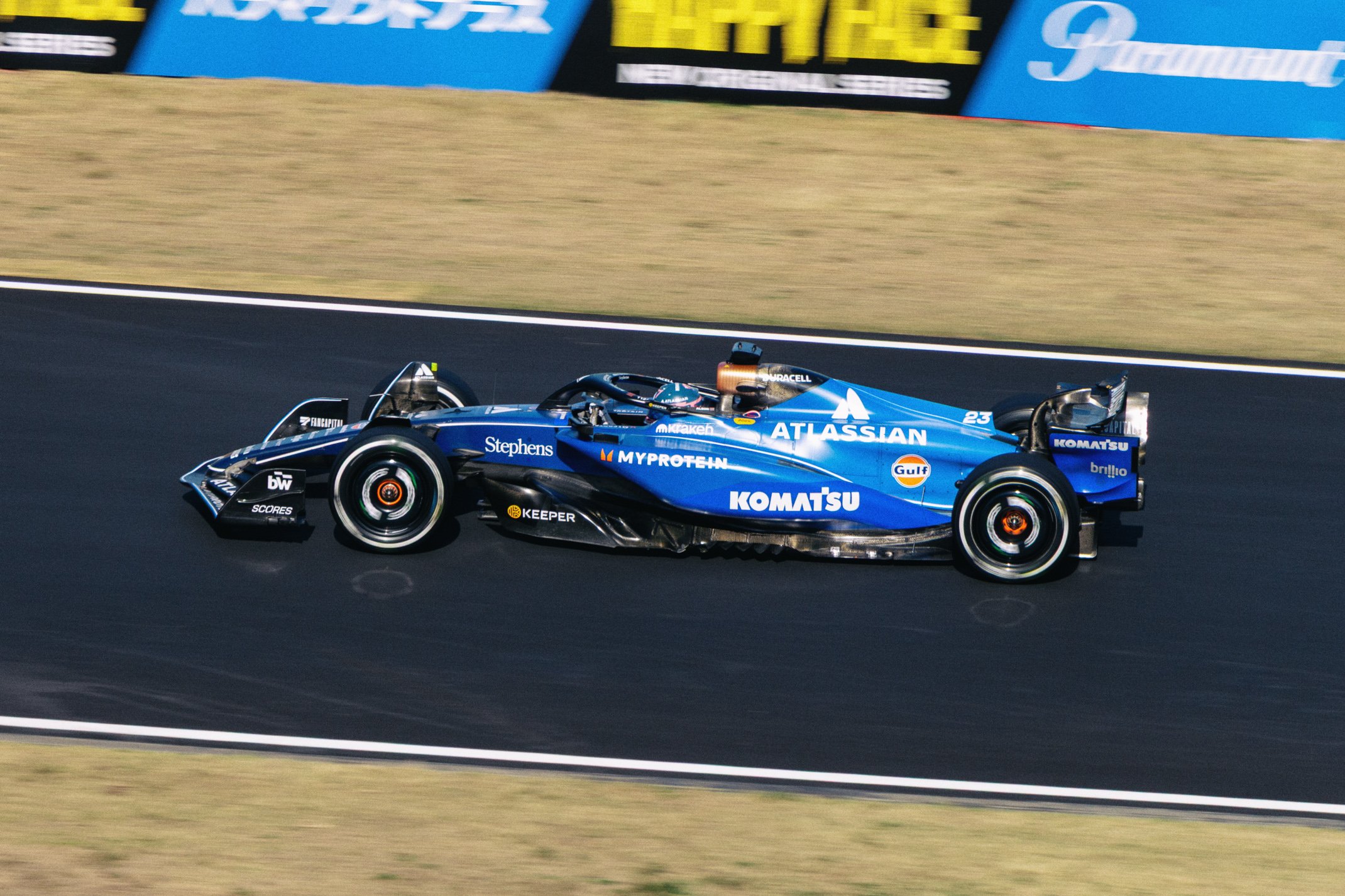 A blue Formula 1 race car on a race track with sponsor logos and advertisements in the background.