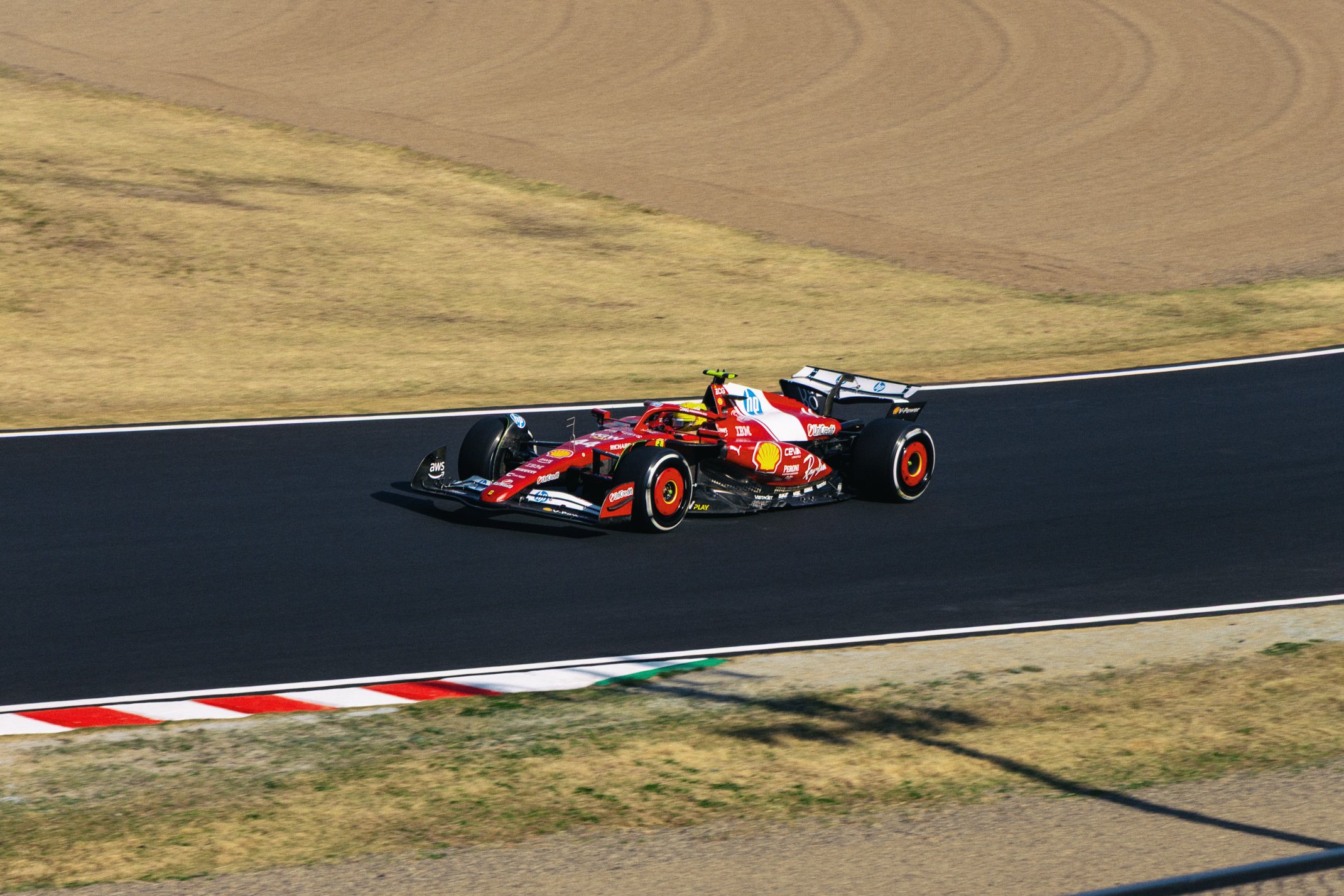 A red Formula 1 race car navigating a turn on a racetrack, with a grassy and dirt background.
