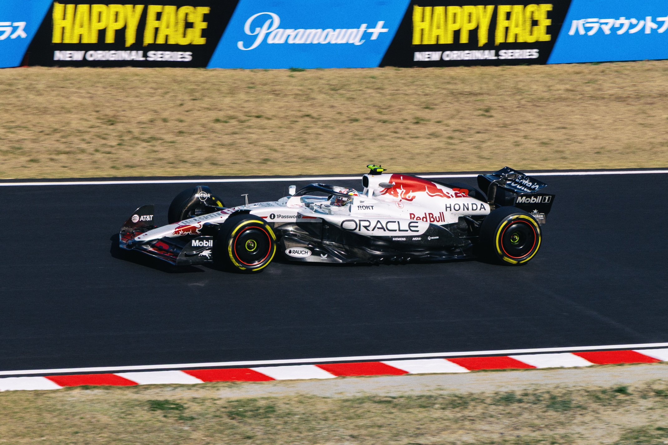 A Honda Formula 1 race car on a racetrack, featuring Red Bull branding and sponsors like Oracle, Mobil 1, and AT&T, with advertisement banners in the background.