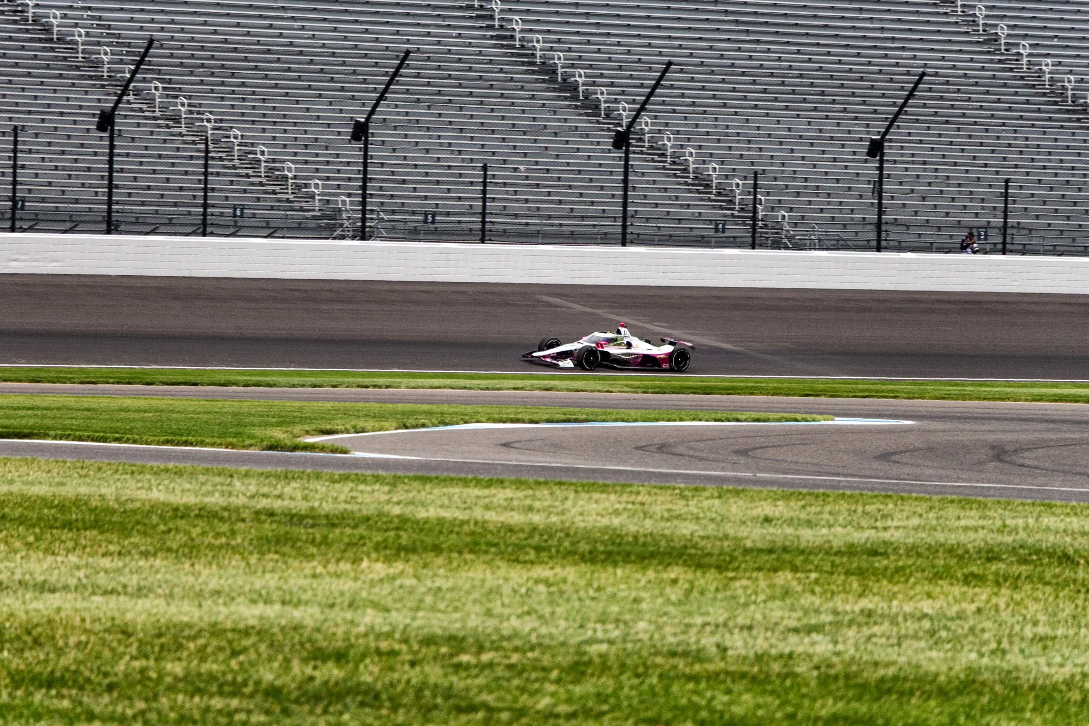A race car on a race track with empty grandstands in the background.