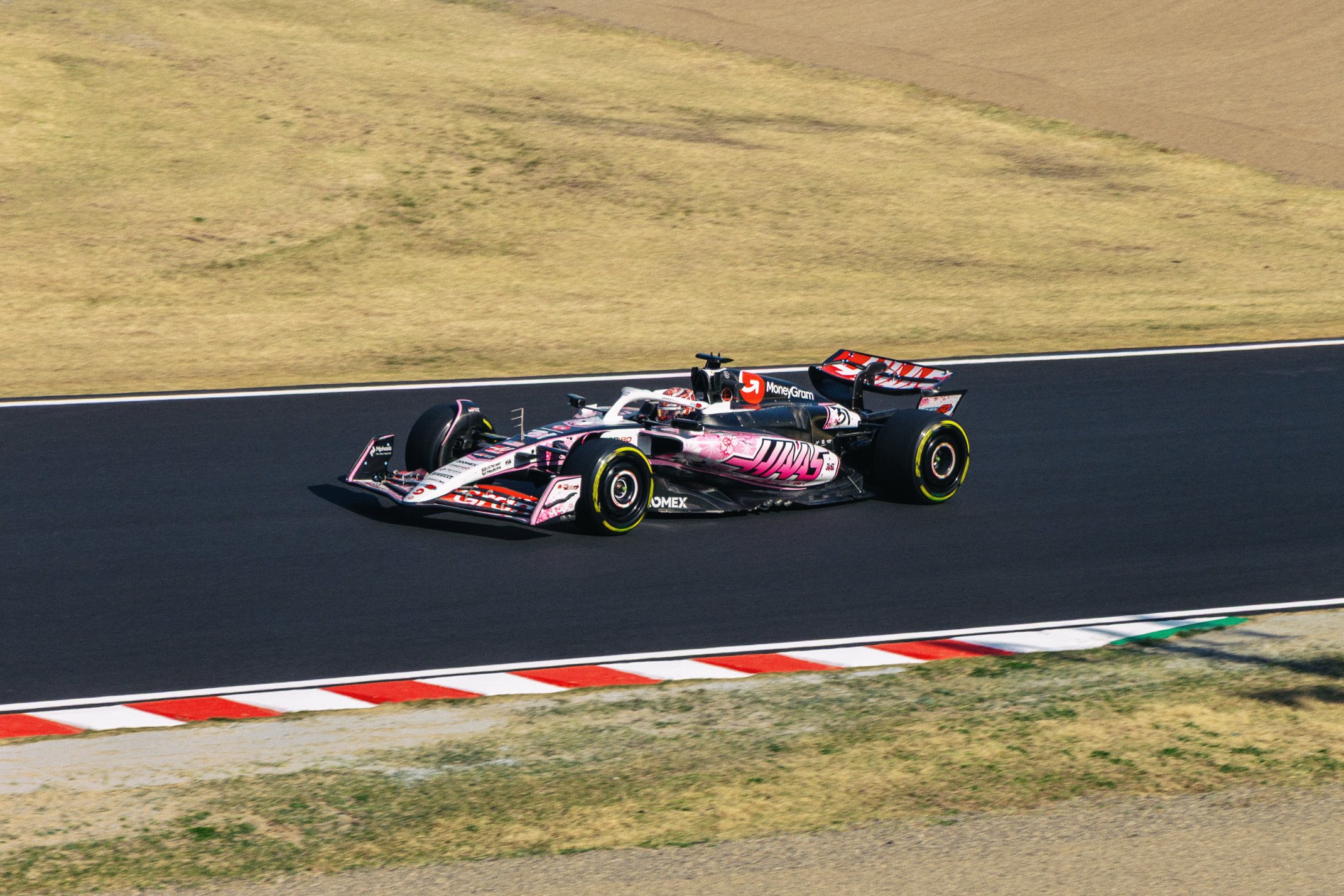 A race car on a track, featuring a primarily white and black design with pink accents, sponsored by MoneyGram and other brands.