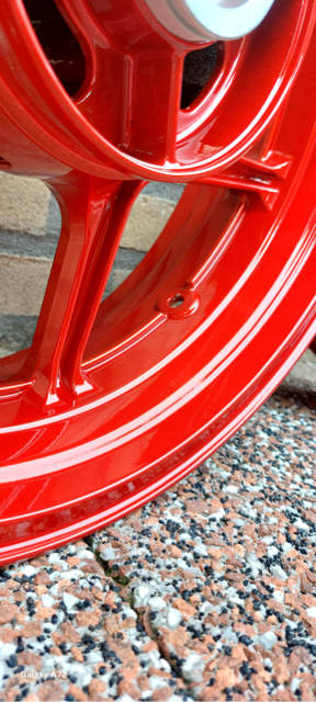 Close-up van een glanzend rood motorvelg tegen een stenen achtergrond.