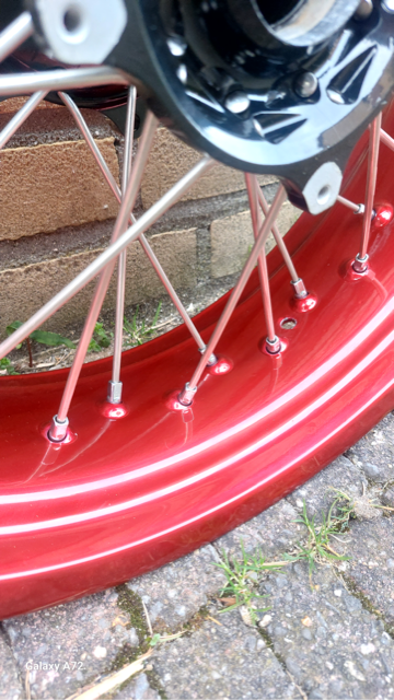 Close-up van het rode wiel van een fiets met spaken en een zwarte naaf, tegen een stenen achtergrond.