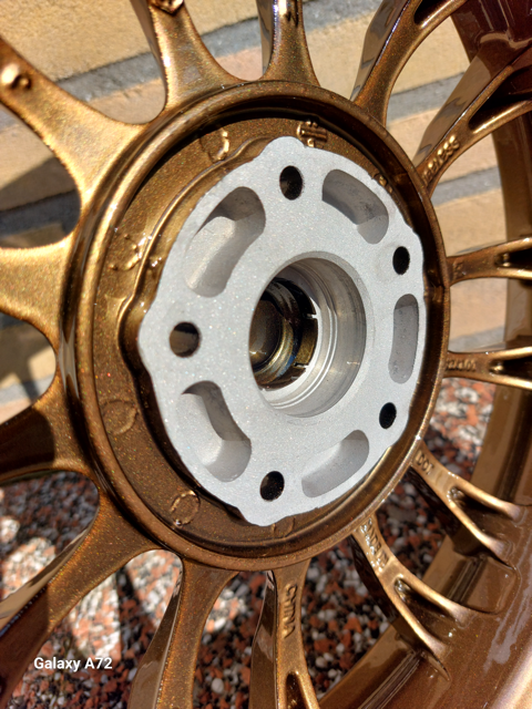 Een detailopname van een goudkleurige velg van een voertuig met spaken, gefotografeerd tegen een bakstenen achtergrond.