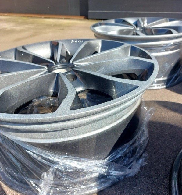 Twee grijze lichtmetalen velgen op een betonnen ondergrond ingepakt in plastic.