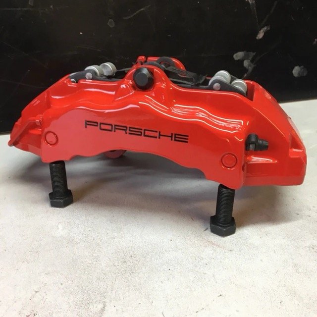 Rode remklauw met Porsche logo op een werkbank.