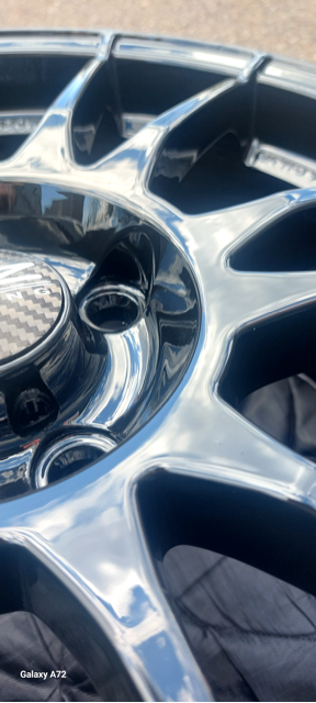 Close-up van een glanzende zwarte autovelg met een koolstofvezel centerkap.