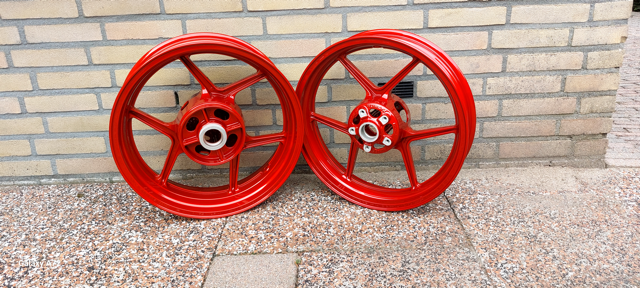 Twee rode fiets- of motorvelgen tegen een bakstenen muur.