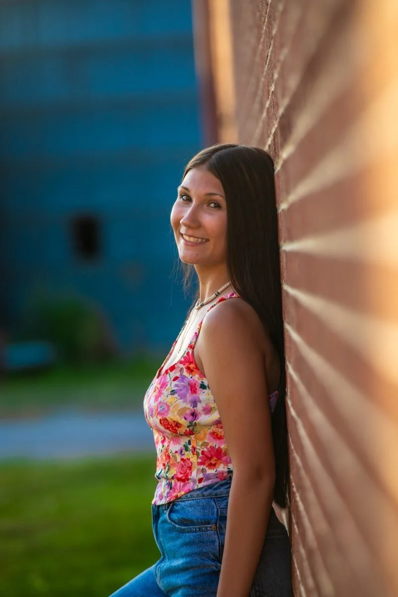 Hailey Clark, poses for a picture against a brick wall in a flower print top