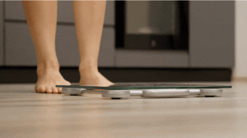 Person standing on a digital bathroom scale on a wooden floor.