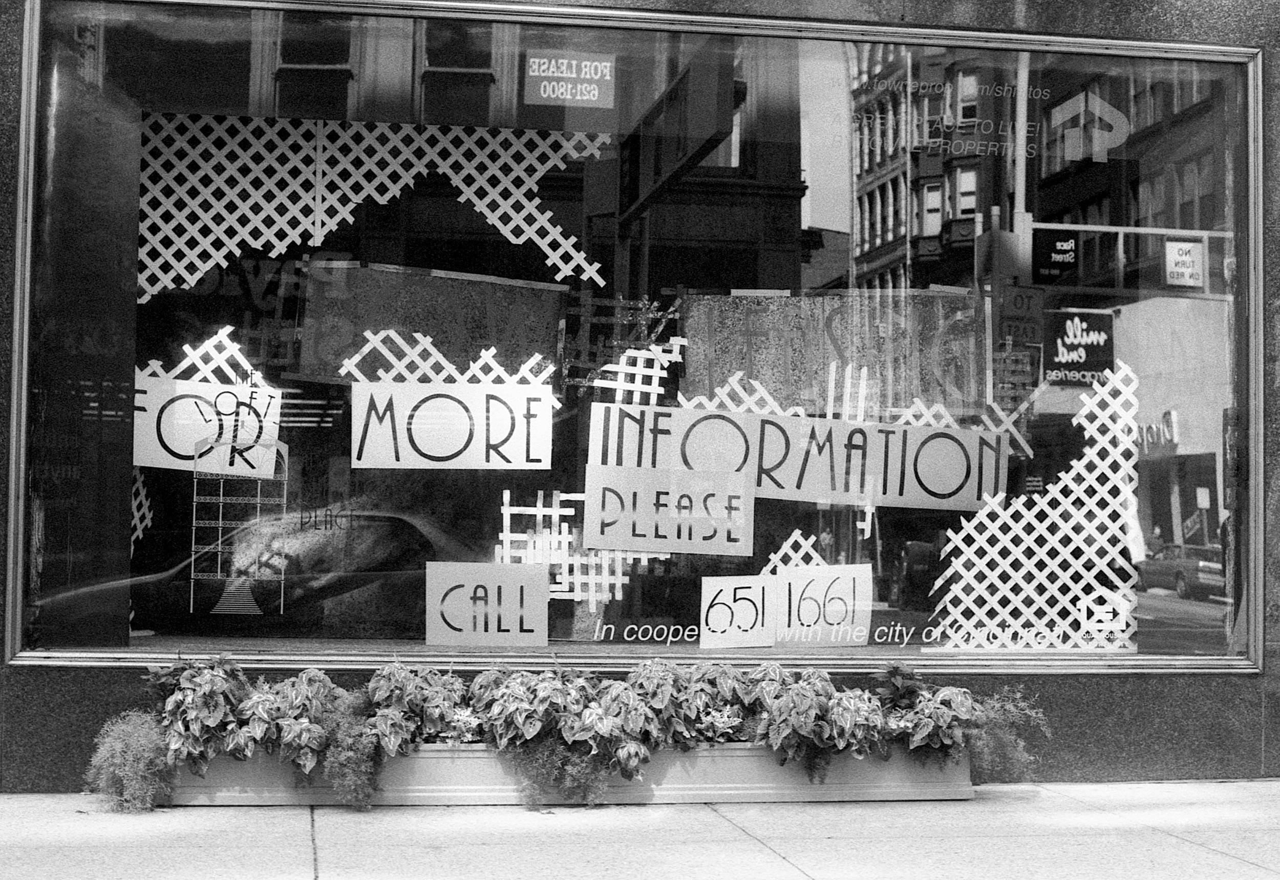 Shop window with signs requesting more information and a phone number, decorated with lattice patterns and flowers at the bottom.
