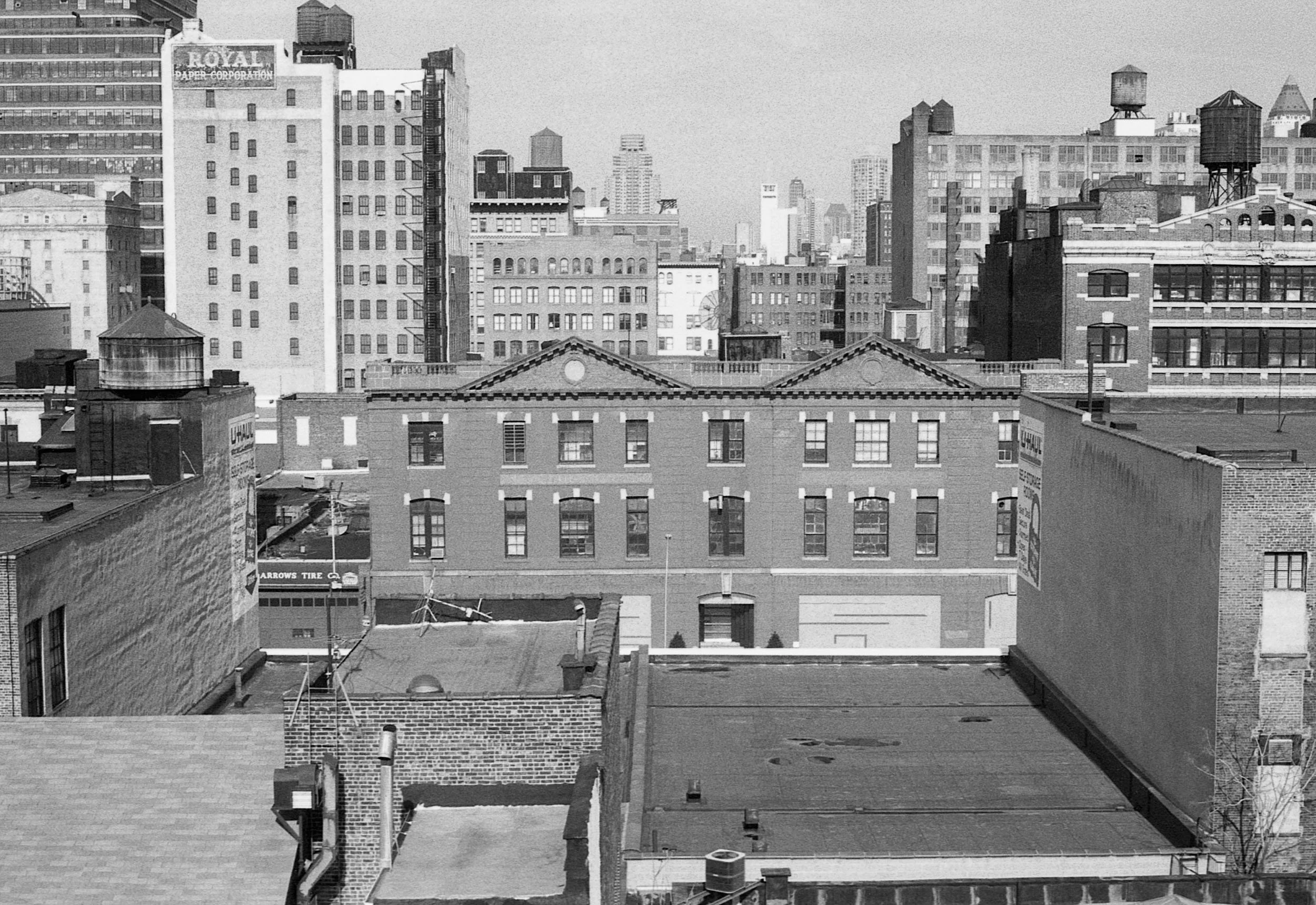 Black and white photo of a city skyline showing multiple tall buildings in the background, with a row of smaller brick buildings in the foreground.