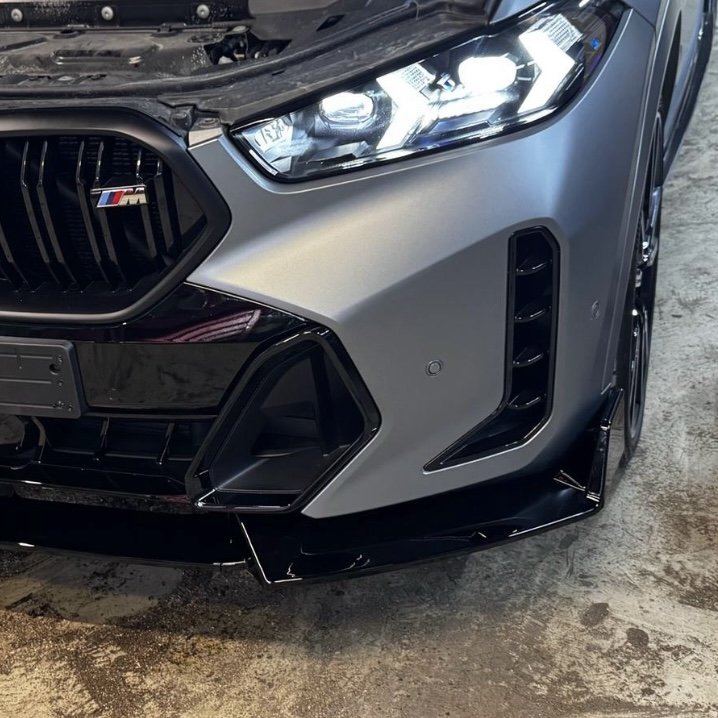 Close-up of a car front bumper and headlight, showcasing the grille and a sports car badge, with visible engine components and sleek design.
