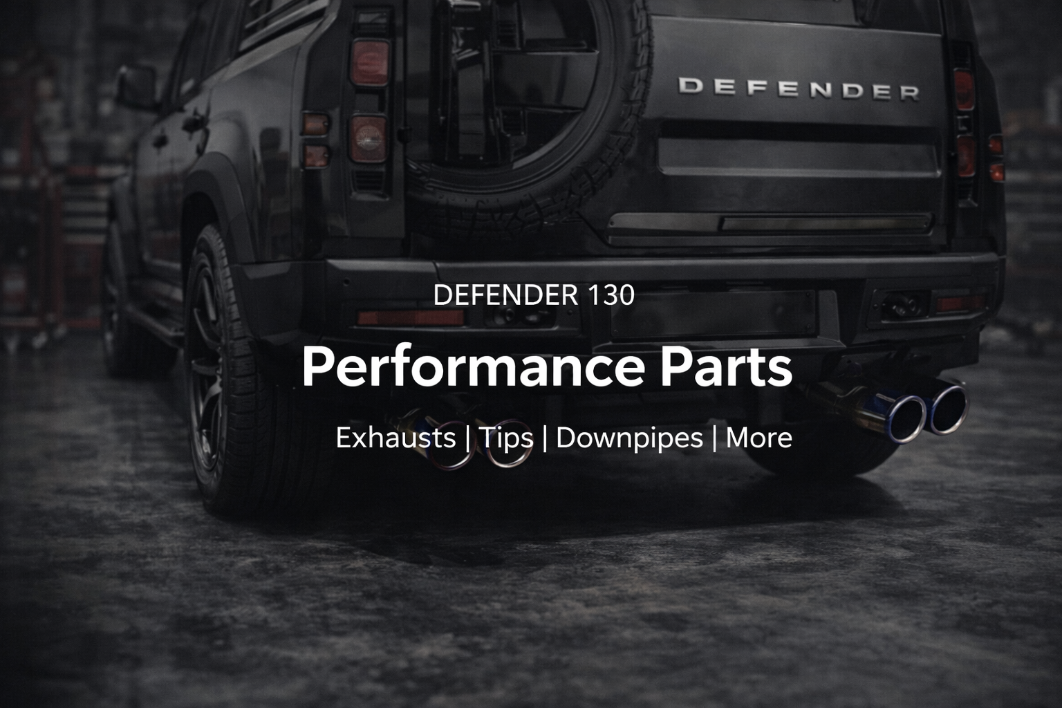 The rear view of a black Land Rover Defender 130 SUV with dual exhaust tips and a spare tire mounted on the back, in a garage or workshop setting. Overlaid text promotes performance parts, including exhausts, tips, downpipes, and more.