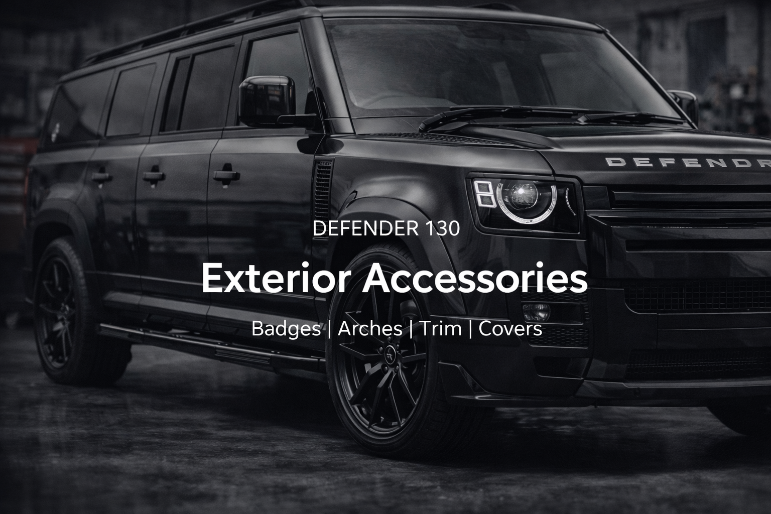 A black Land Rover Defender 130 vehicle in a garage with text overlay that reads 'DEFENDER 130 Exterior Accessories Badges Arches Trim Covers'.