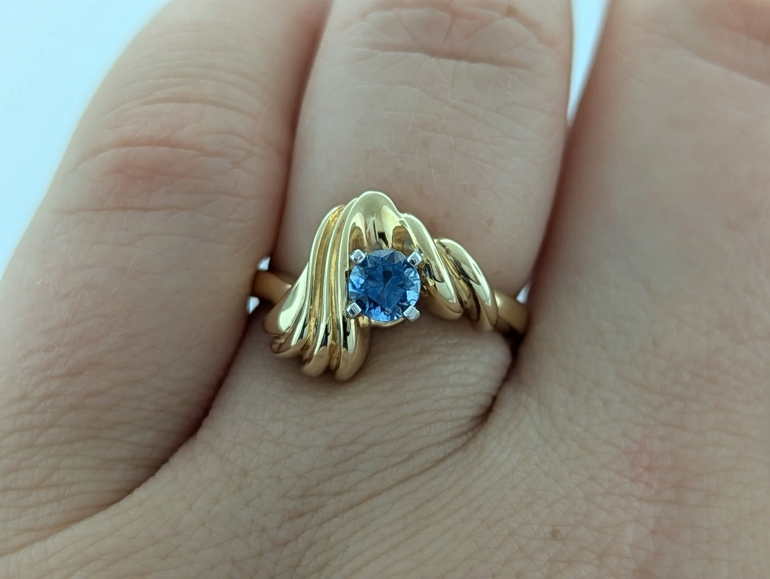 1.02ct round cut Montana Sapphire ring set in a unique 14k yellow gold freeform design, showcasing elegant curves and a rich blue gemstone.
