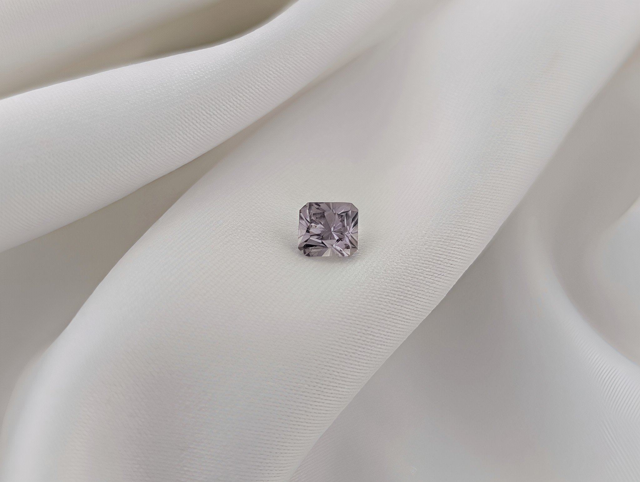 Radiant cut grey sapphire displayed on white silk