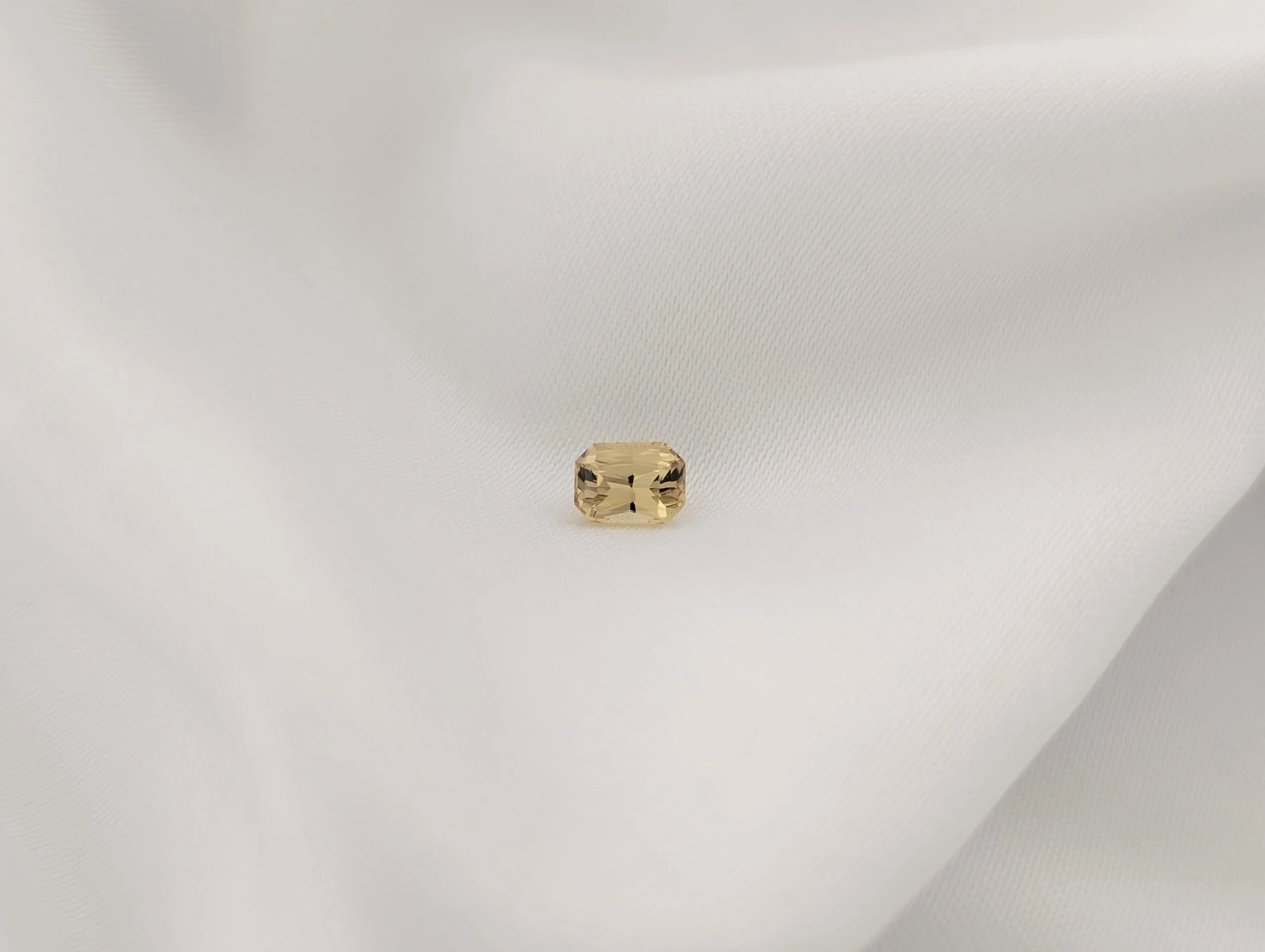 Radiant cut yellow sapphire displayed on white silk