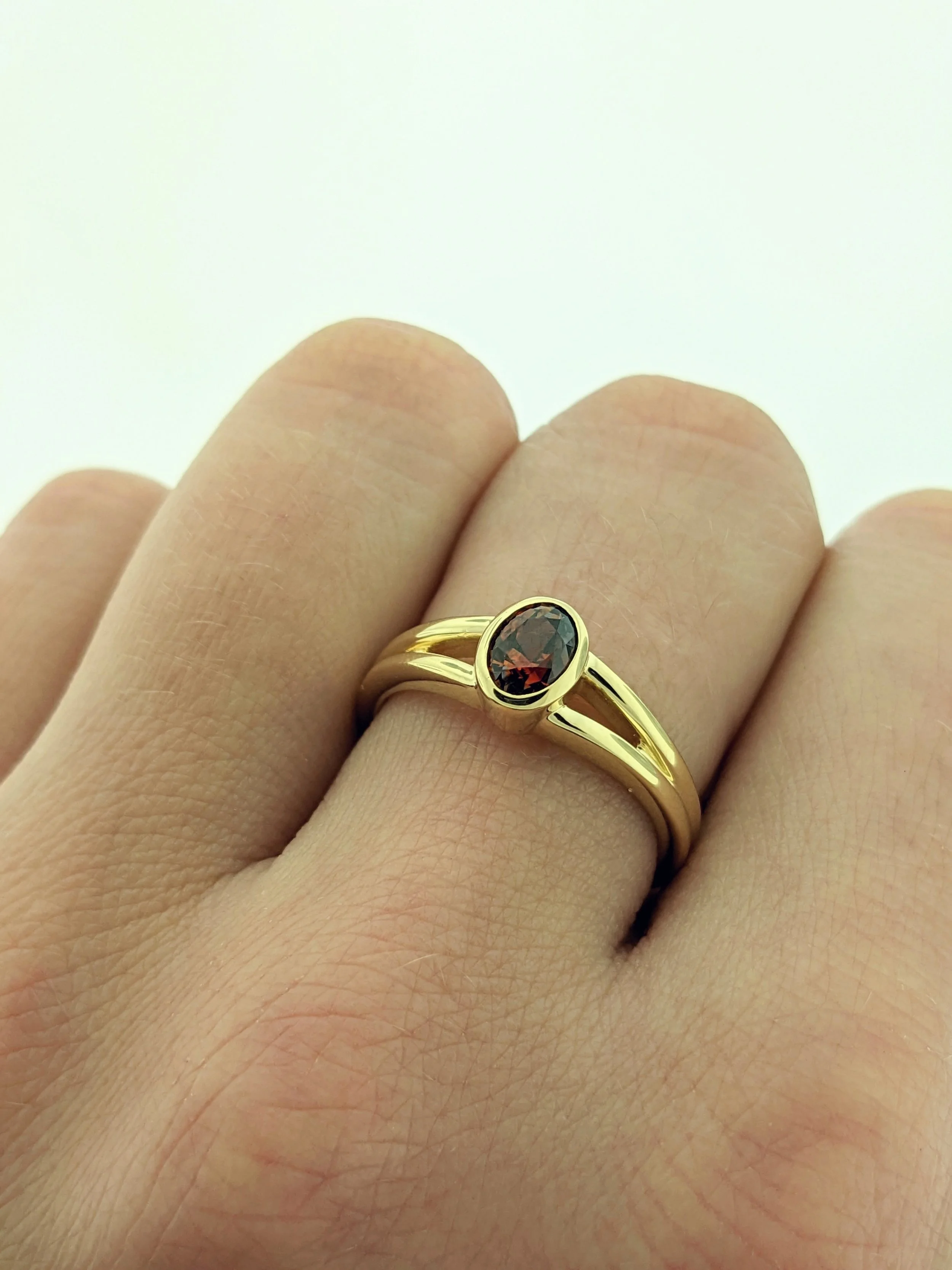 0.81ct deep orange oval cut Montana Sapphire bezel set ring with split band in 14k yellow gold.