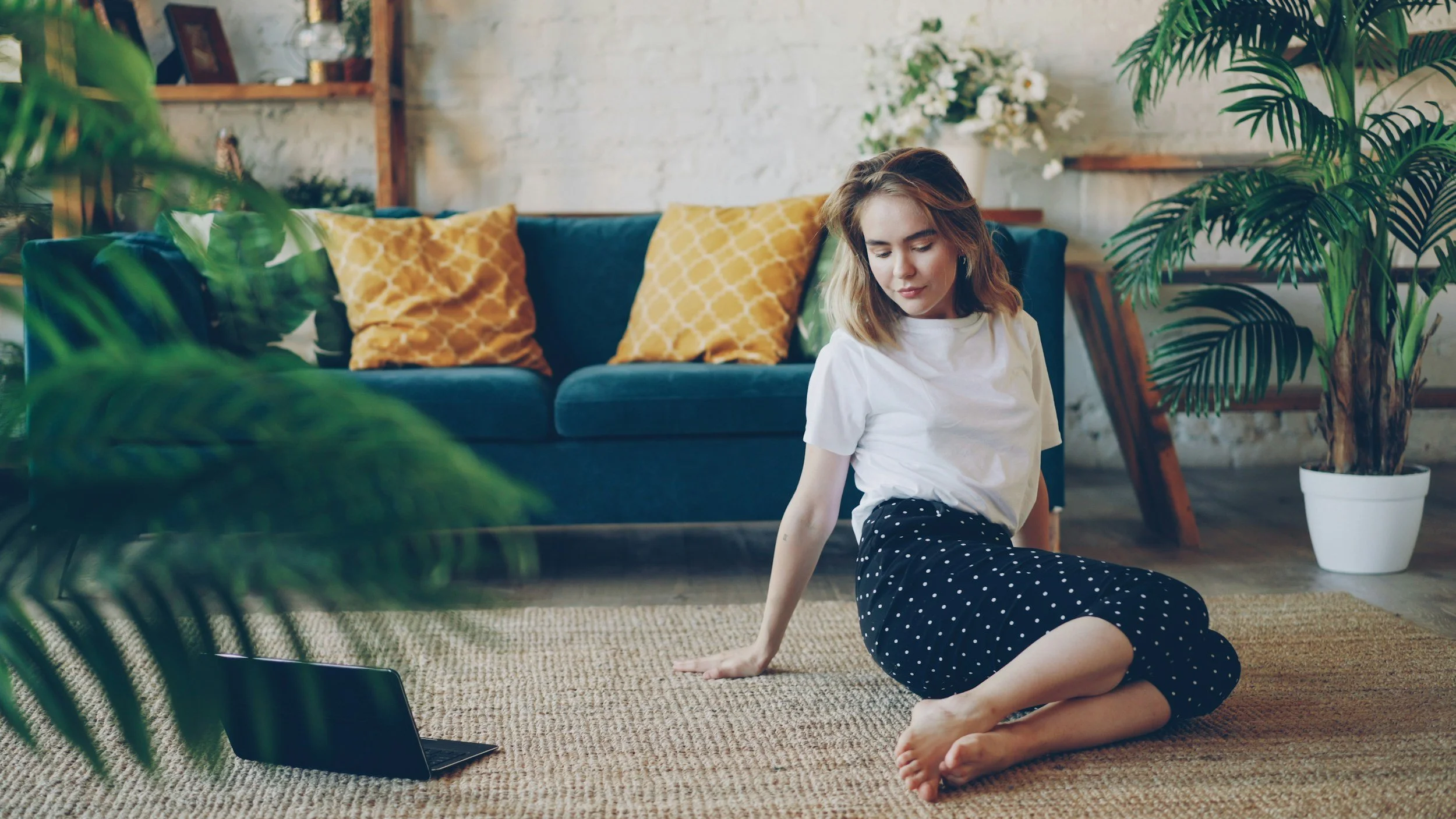 Woman sitting on the floor of a bright living room, resting against a couch
