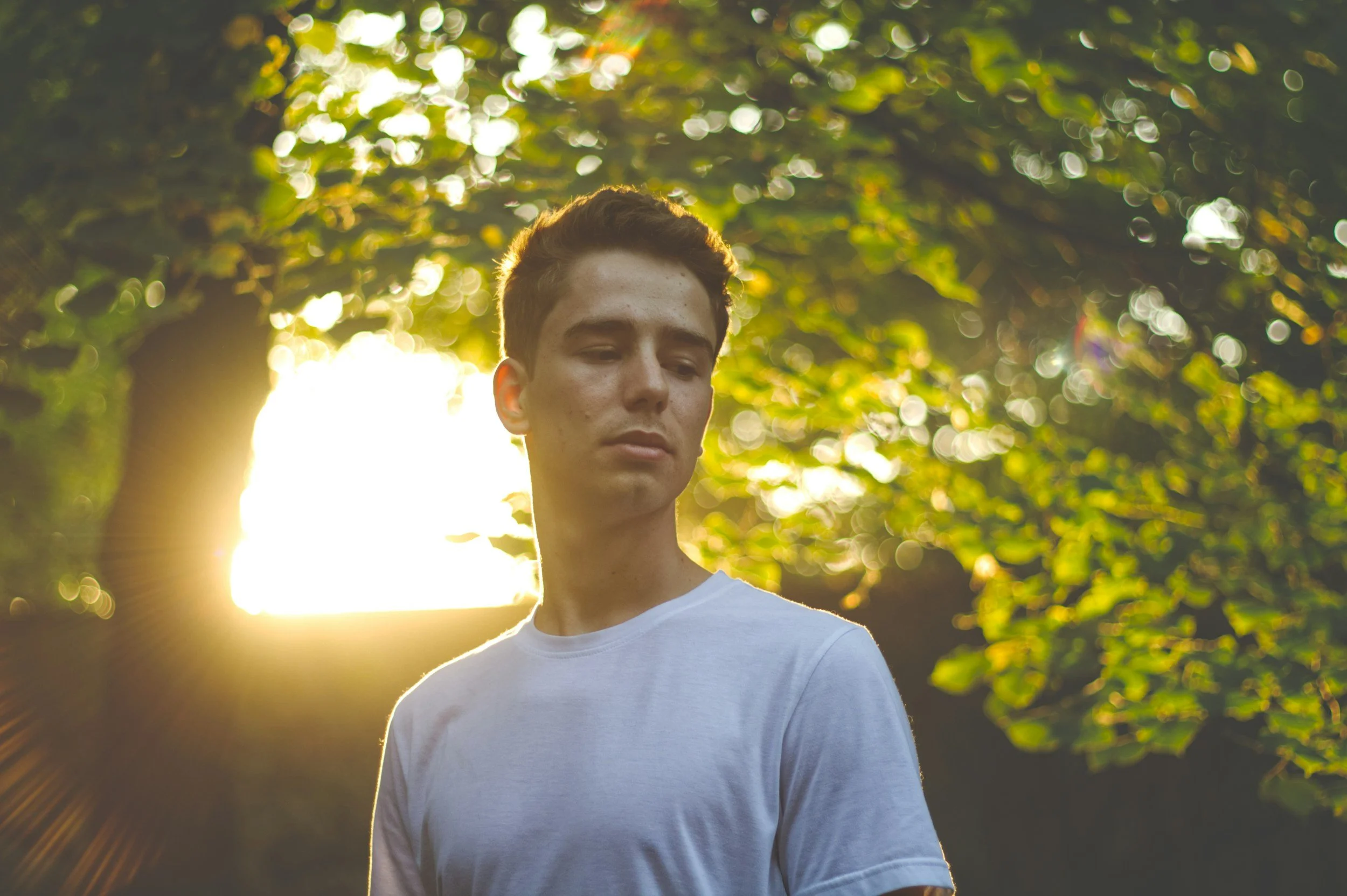 Man standing outdoors with his eyes closed, sunlight coming through the trees