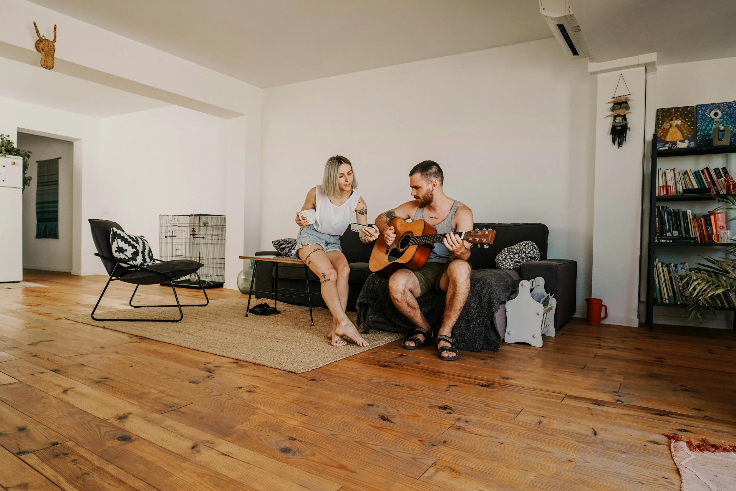 Couple sitting together on the floor of their living room, one playing guitar