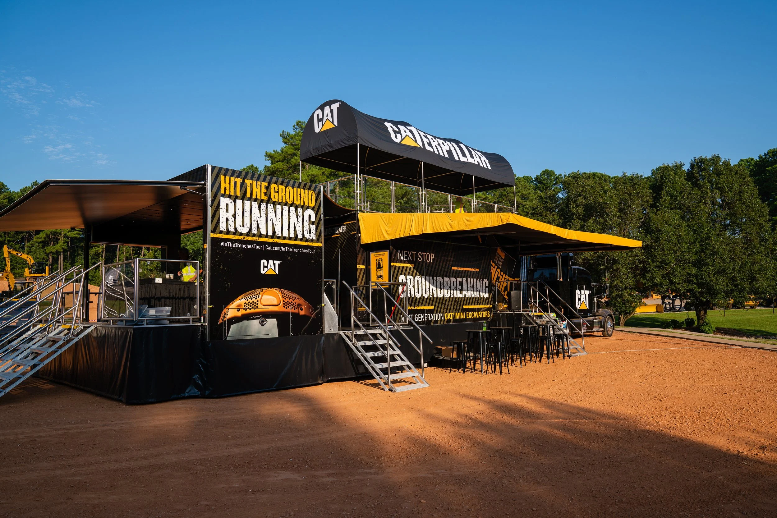 Outdoor Caterpillar promotional setup with banners and seating, featuring "Hit the Ground Running" slogan and CAT branding.