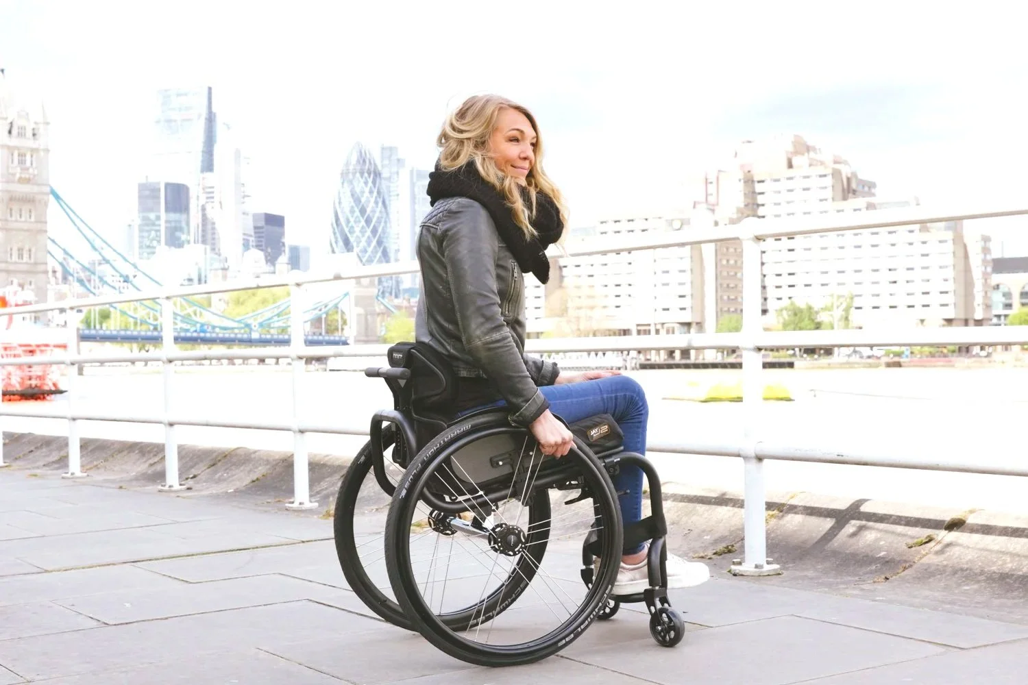A woman in a wheelchair on a city sidewalk with a skyline background.