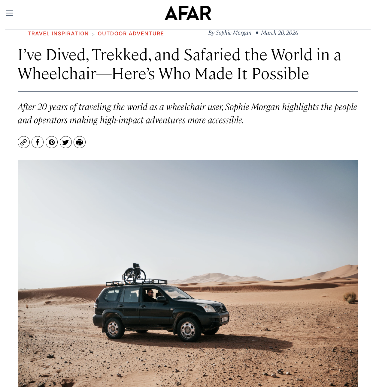 A black SUV with a wheelchair mounted on the roof, parked on a sandy desert landscape with sand dunes under a clear sky.