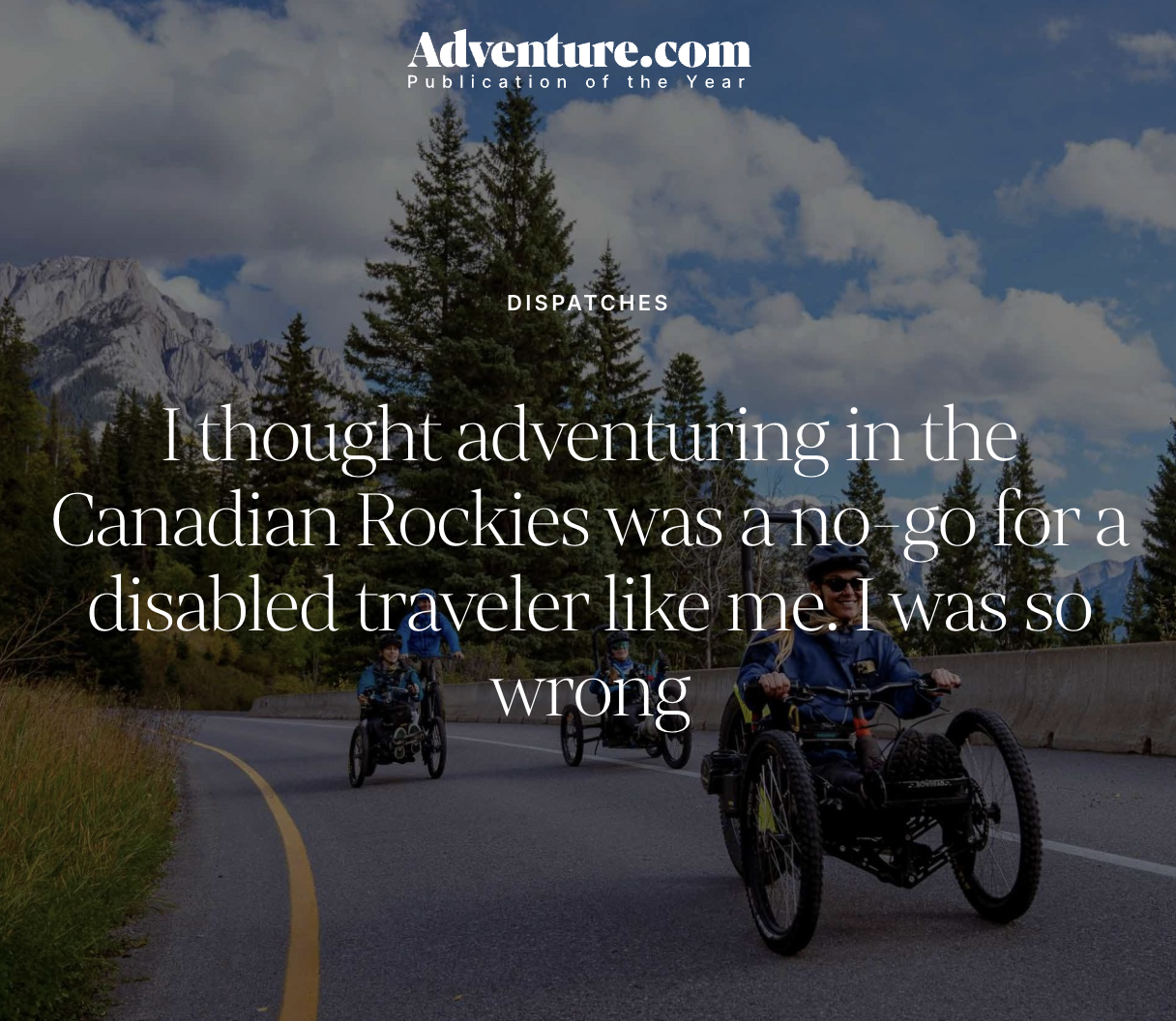 People riding fat tire bikes on a mountain road with trees and mountains in the background, under a partly cloudy sky.