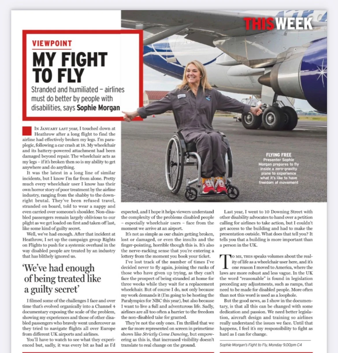 A woman in a wheelchair smiling and posing on an airport tarmac in front of a large airplane, with her arms outstretched and wearing a gray jumpsuit.