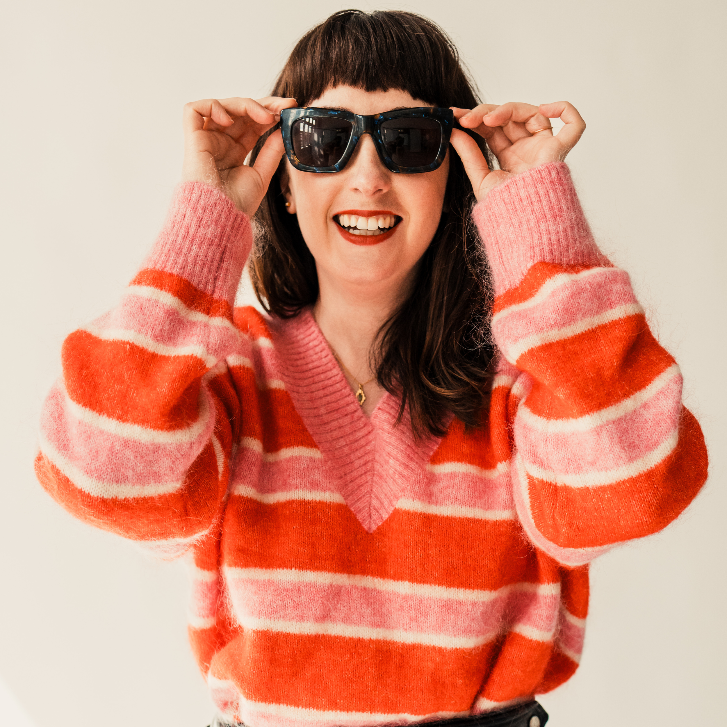 Person wearing sunglasses and a red and pink striped sweater, smiling.