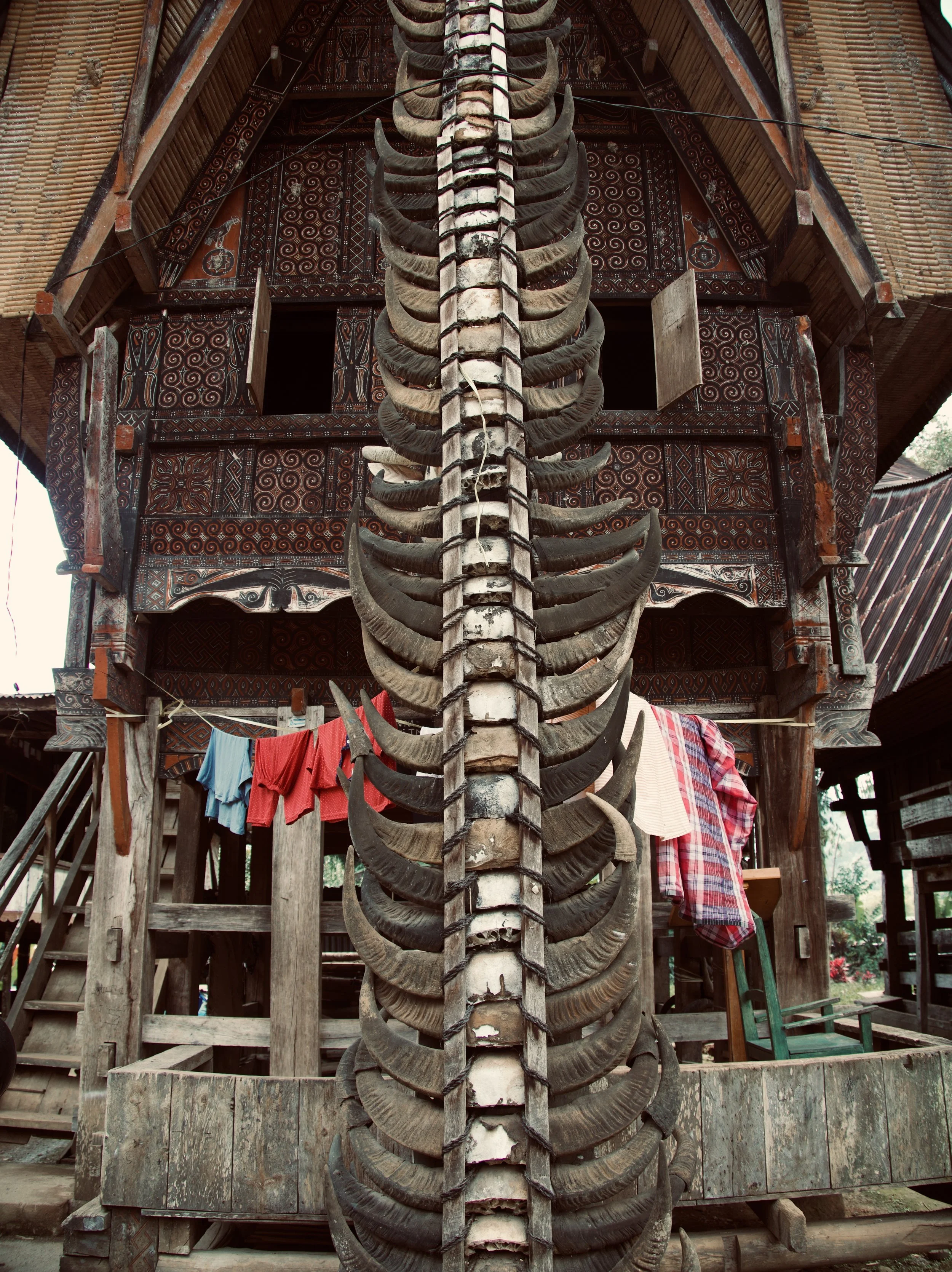 Traditional Balinese house with ornate wooden carvings and dangling clothing, featuring large animal horns or antlers as decoration.