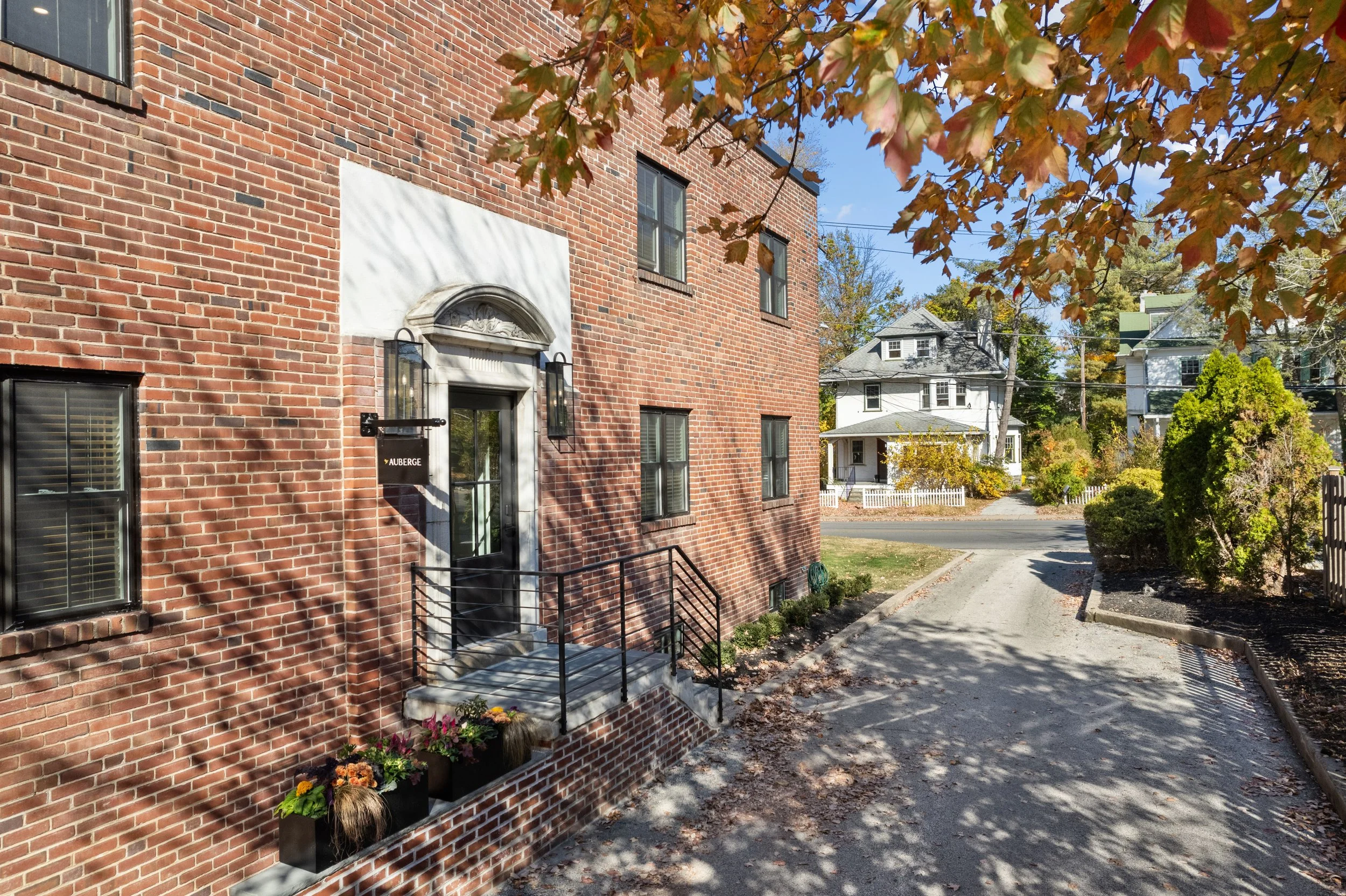Exterior of Auberge, featuring the red brick apartment building with black window frames, a white stone doorway with a black door, and small flower pots on a brick ledge in front.