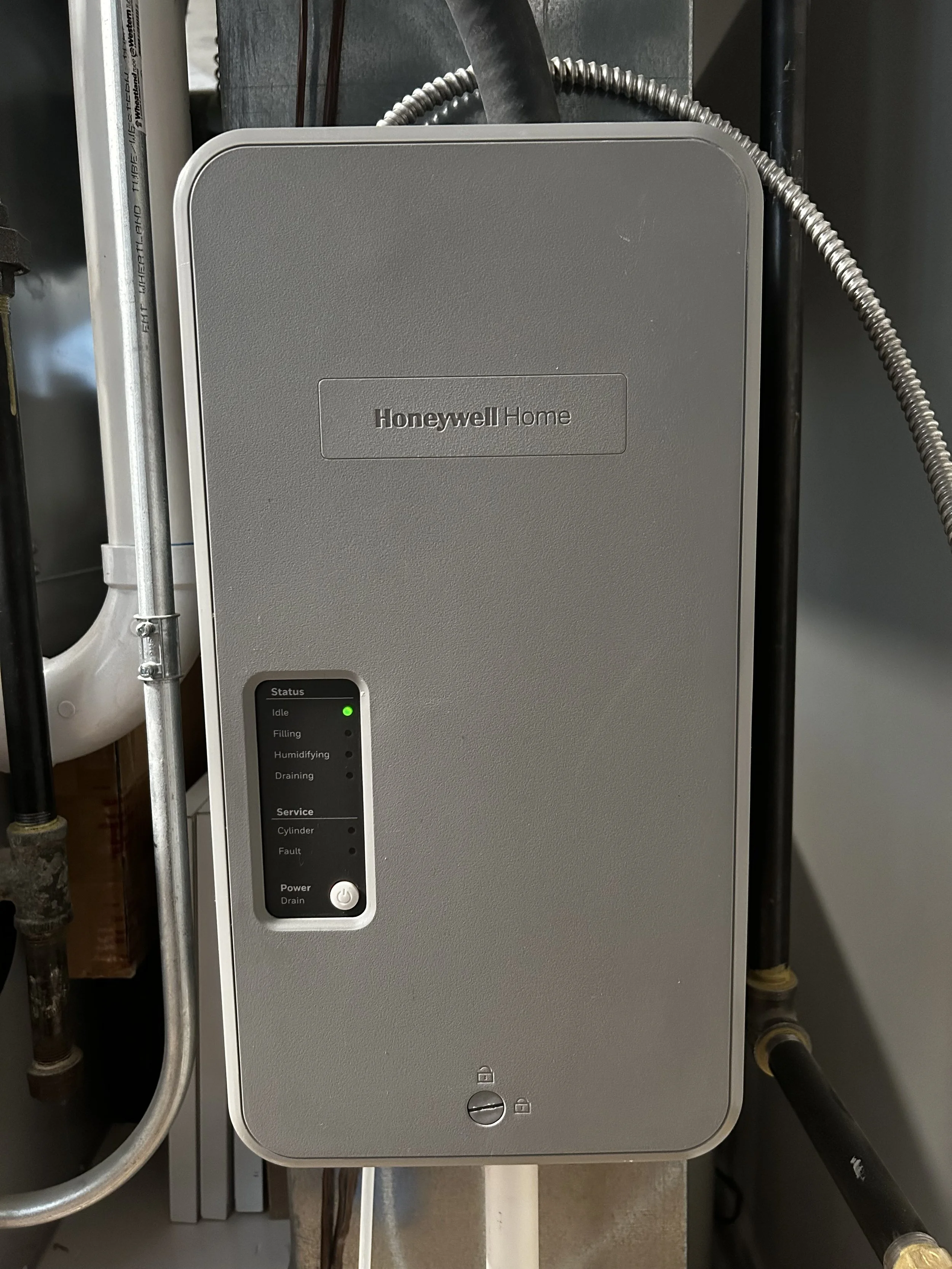 A Honeywell Home Humidifier control unit with status indicator lights and power button, installed in a utility room.