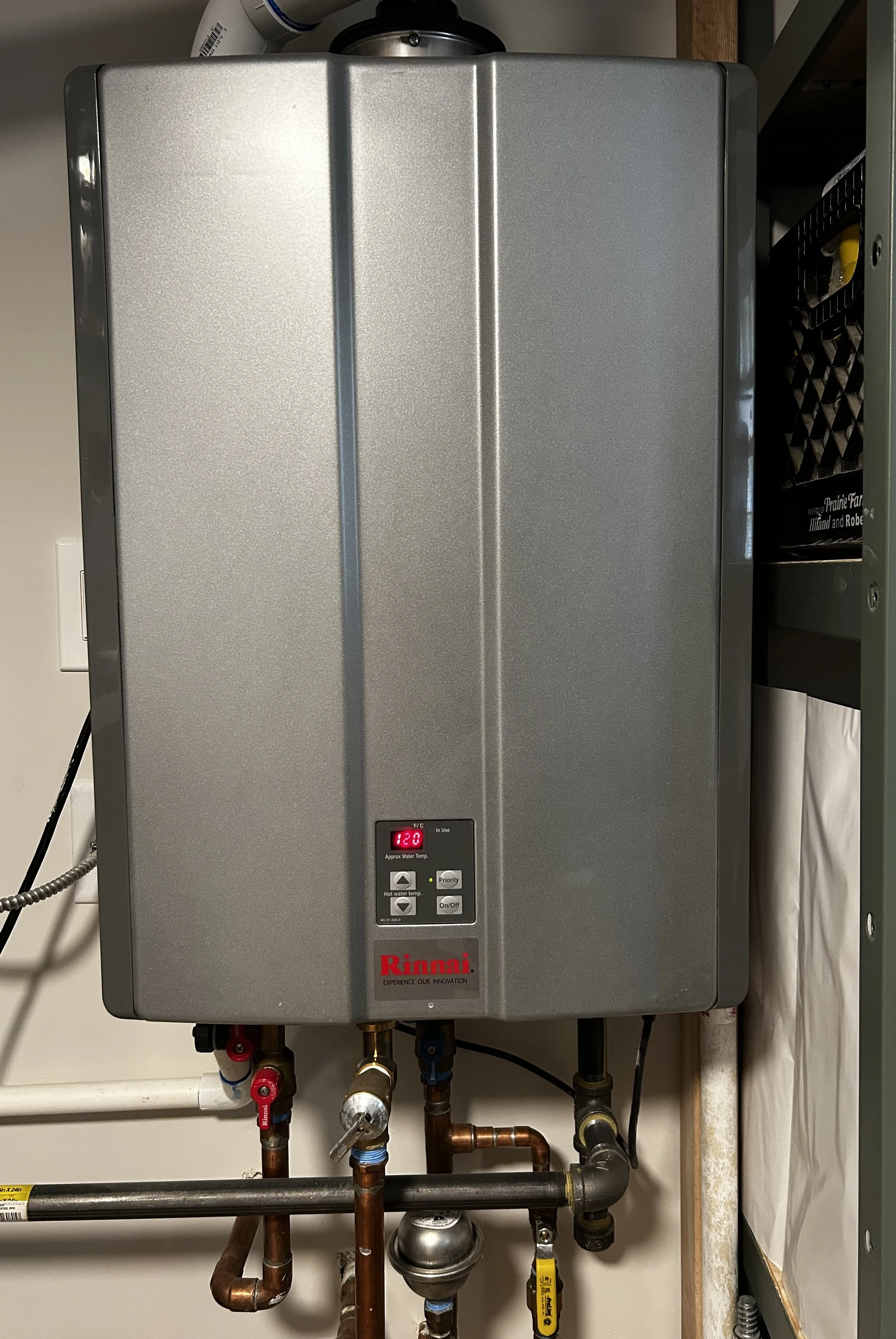 A wall-mounted Rinnai tankless water heater with a digital display, pipes, and valves underneath.