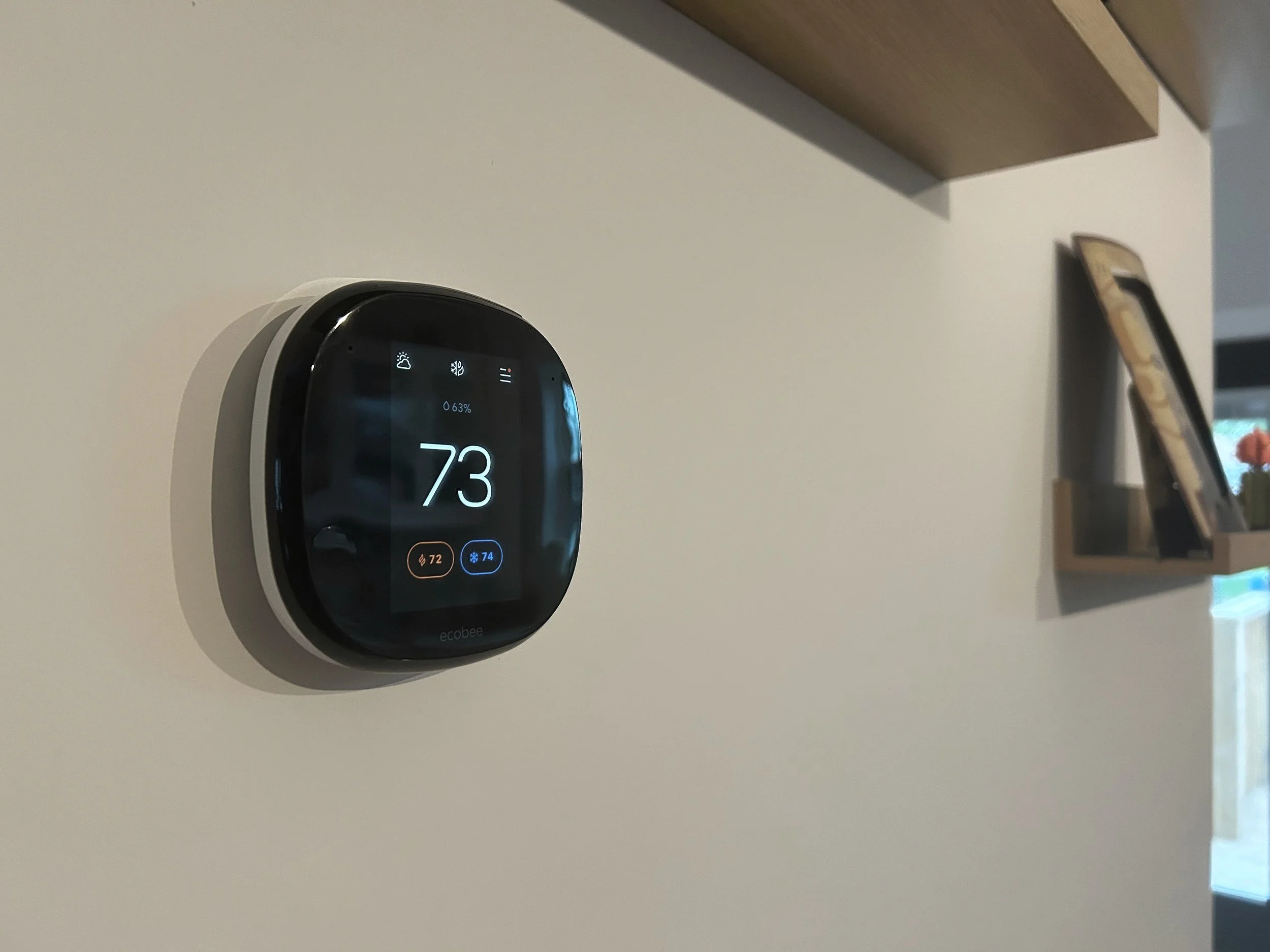 Smart thermostat on a wall displaying a temperature of 73 degrees Fahrenheit, with icons indicating humidity, fan, and other settings.