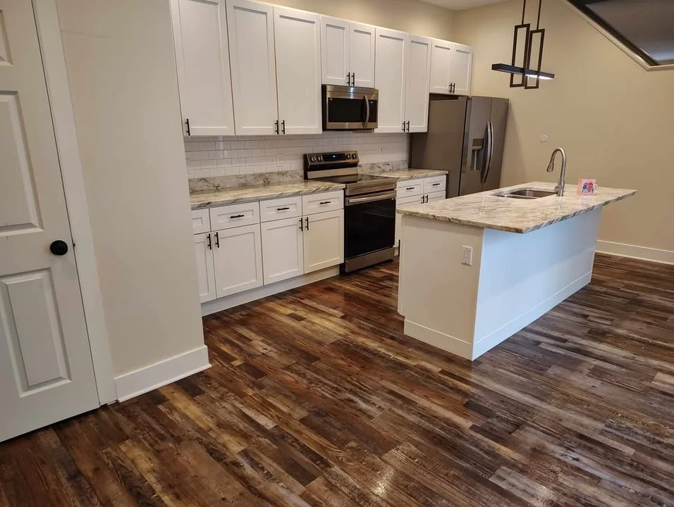 Kitchen with white cabinets, granite countertops, stainless steel appliances, and wood flooring.