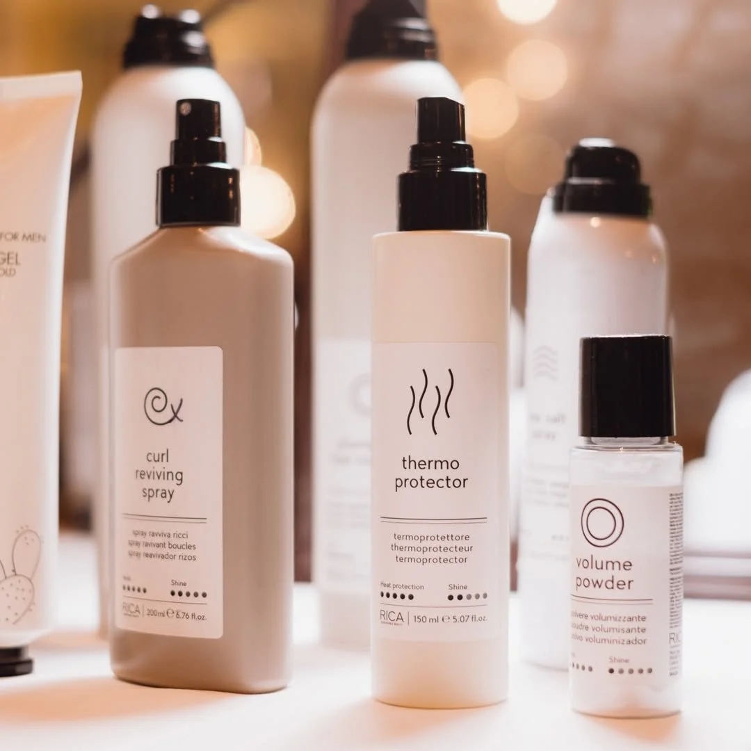 Produits de soins capillaires, notamment un spray revitalisant pour boucles, un thermoprotector et une poudre volumisante, sur une surface blanche.