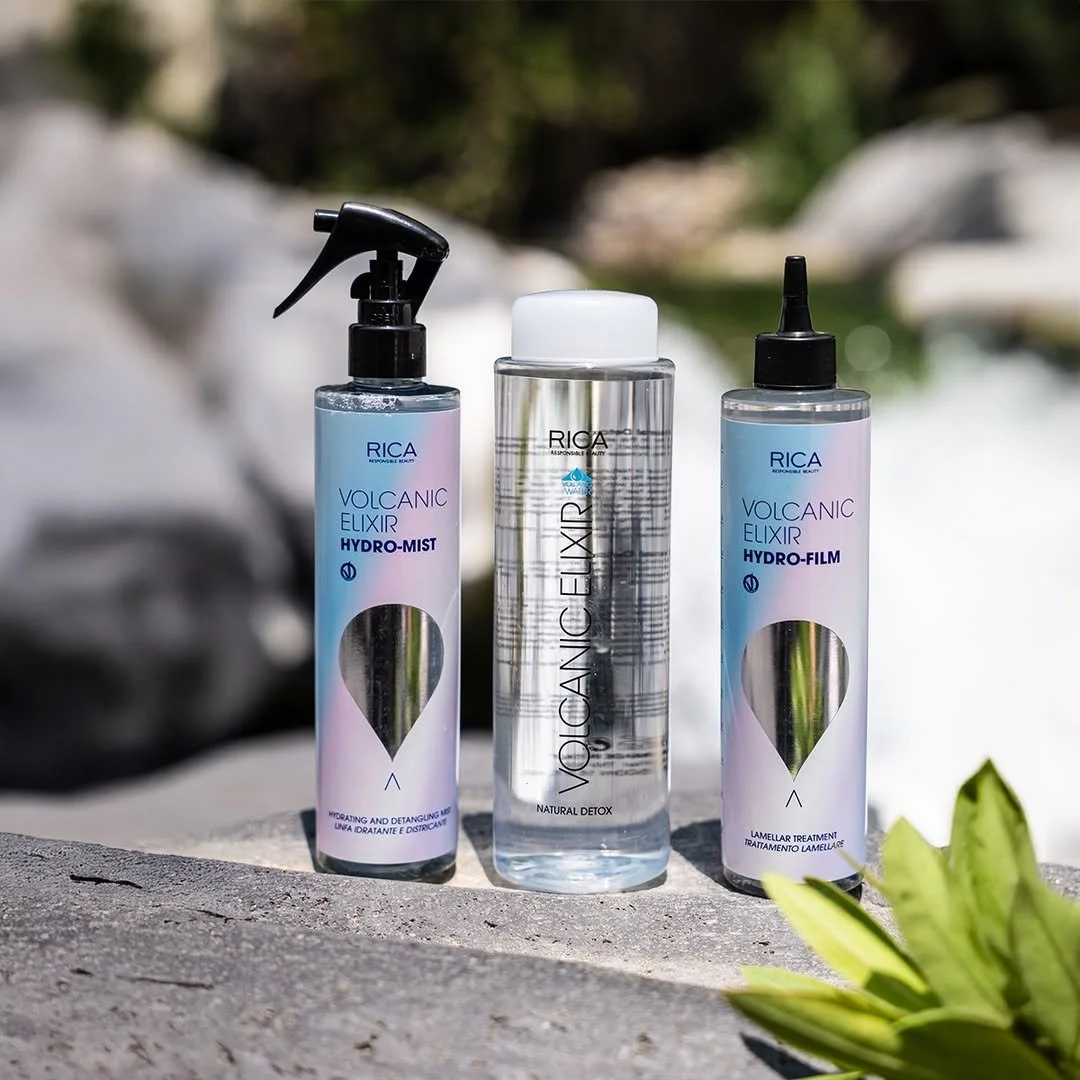 Trois flacons de produits pour la peau de la marque RICA, comprenant deux flacons de Elixir Volcanic, un Hydro-Mist et un Hydro-Film, posés sur une surface en pierre avec un fond naturel flou.