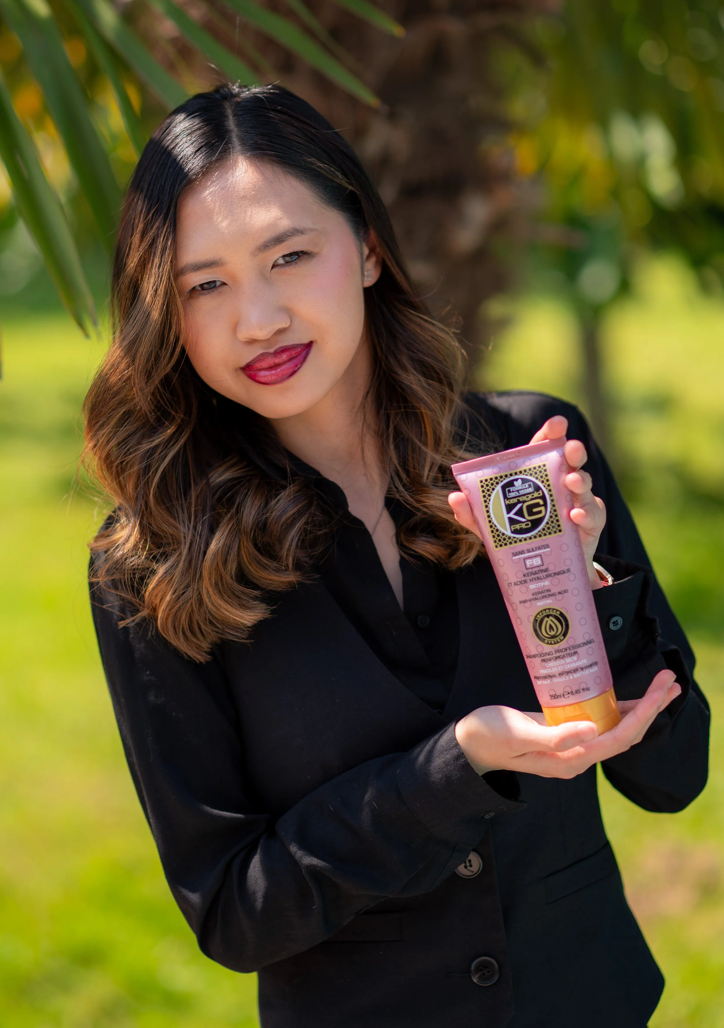 Une femme tient une tube de soins capillaires dans un environnement extérieur avec des arbres en arrière-plan.