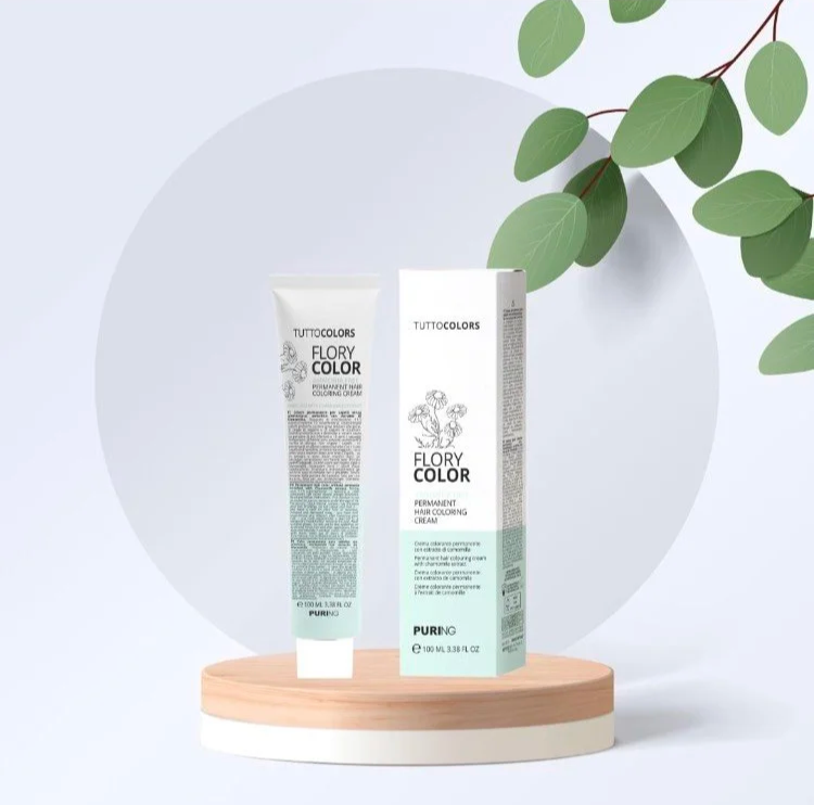 Tube de crème de coloration capillaire et son emballage, placés sur un support en bois, avec des feuilles vertes en arrière-plan.