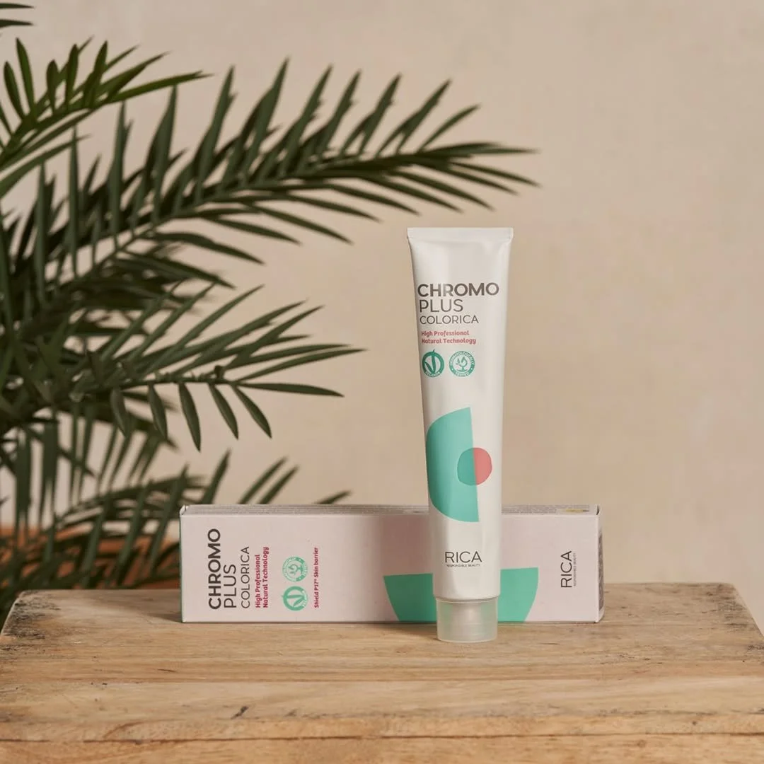 Tube de crème ou de gel blanc avec des graphiques verts et rouges, placé devant une boîte orange et blanche, sur une surface en bois, avec des feuilles vertes à gauche, fond beige.