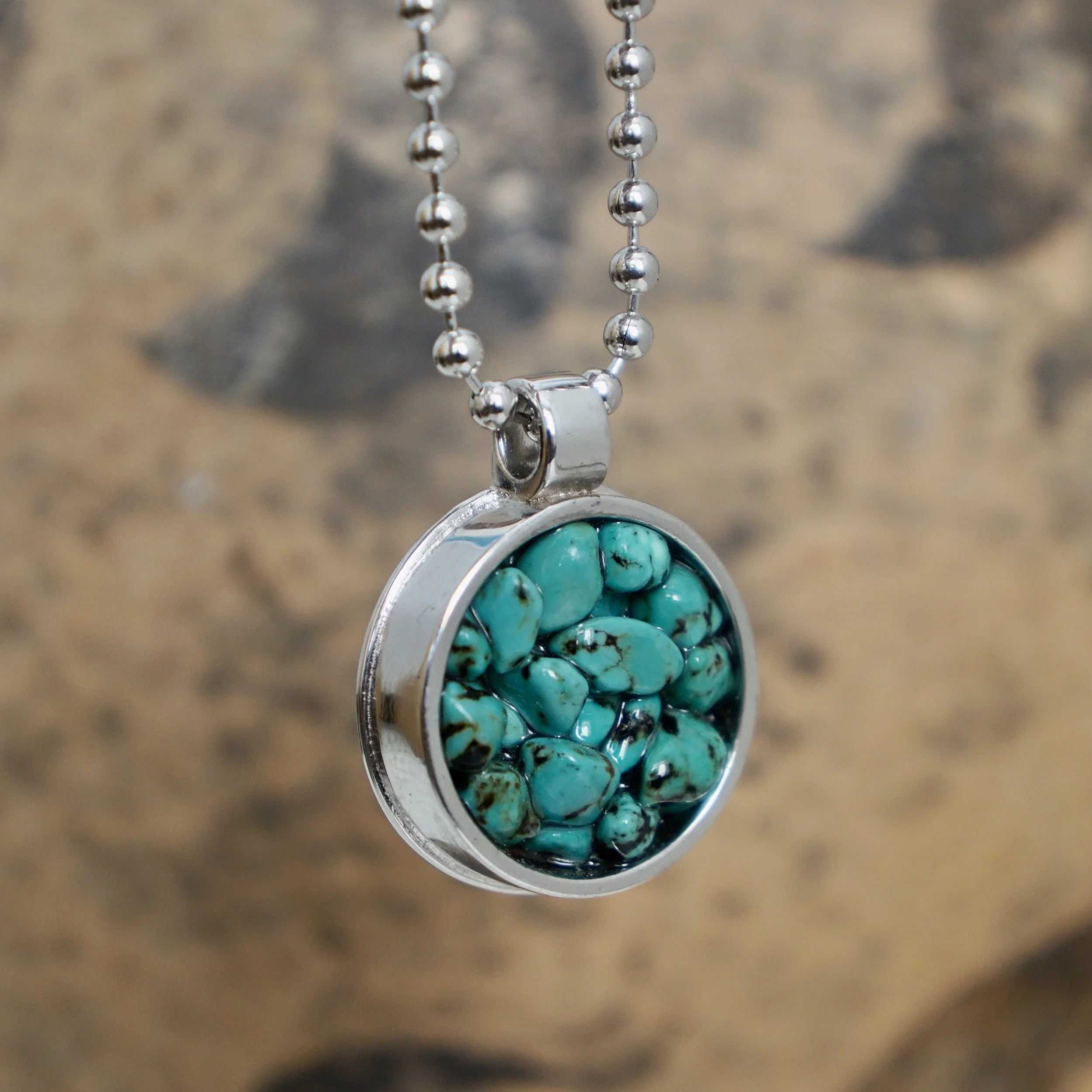 A silver necklace with a round pendant filled with small turquoise stones.