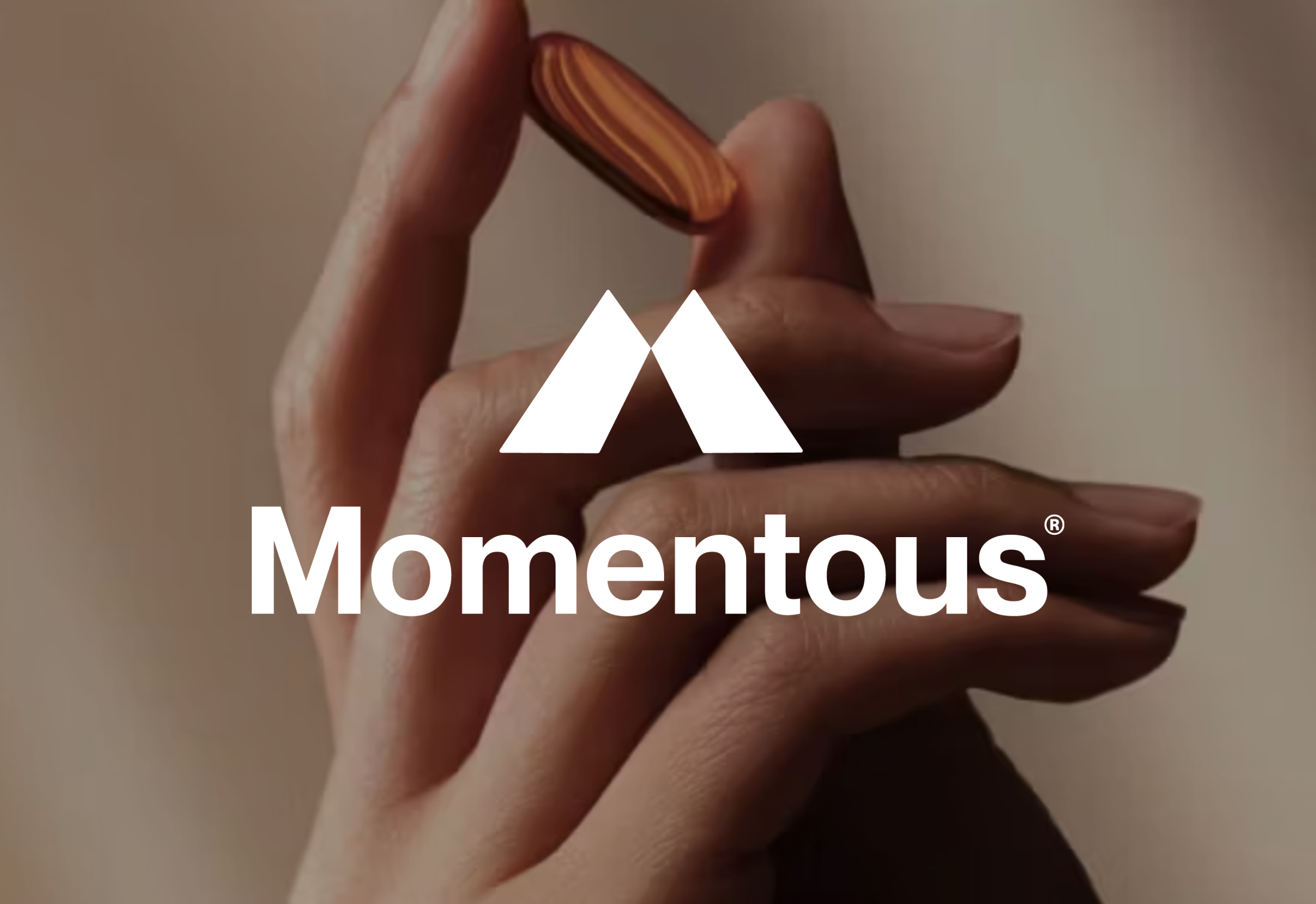 Close-up of a person's hand holding a small, striped, brown and orange object, with the white logo and text 'Momentous' overlaid.