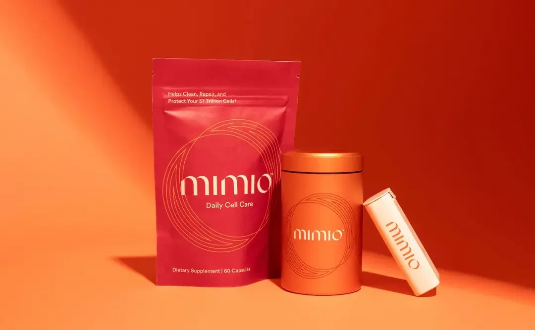 Red package of dietary supplements labeled 'MIMIO Daily Cell Care,' an orange container with the same branding, and a white cylindrical product with 'MIMIO' branding, against an orange background.