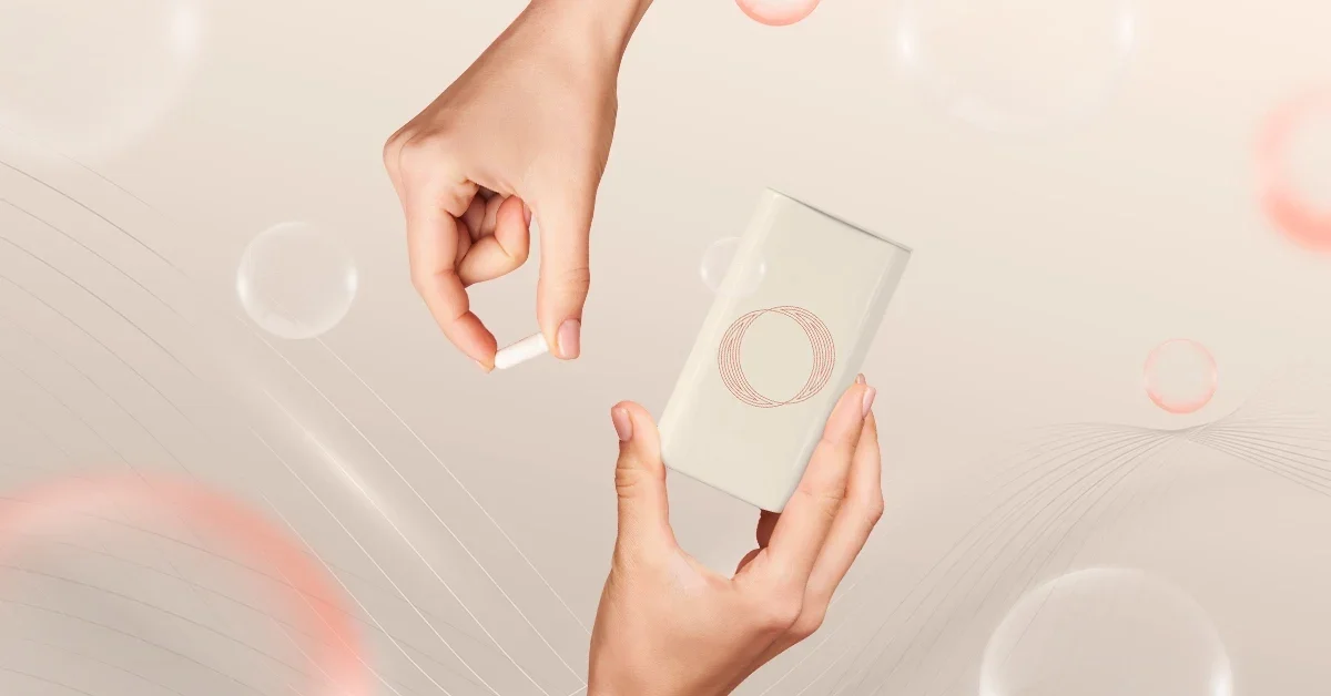 A person’s hand placing a white pill capsule into a white mug with a circular design, against a beige background with floating bubbles and abstract lines.