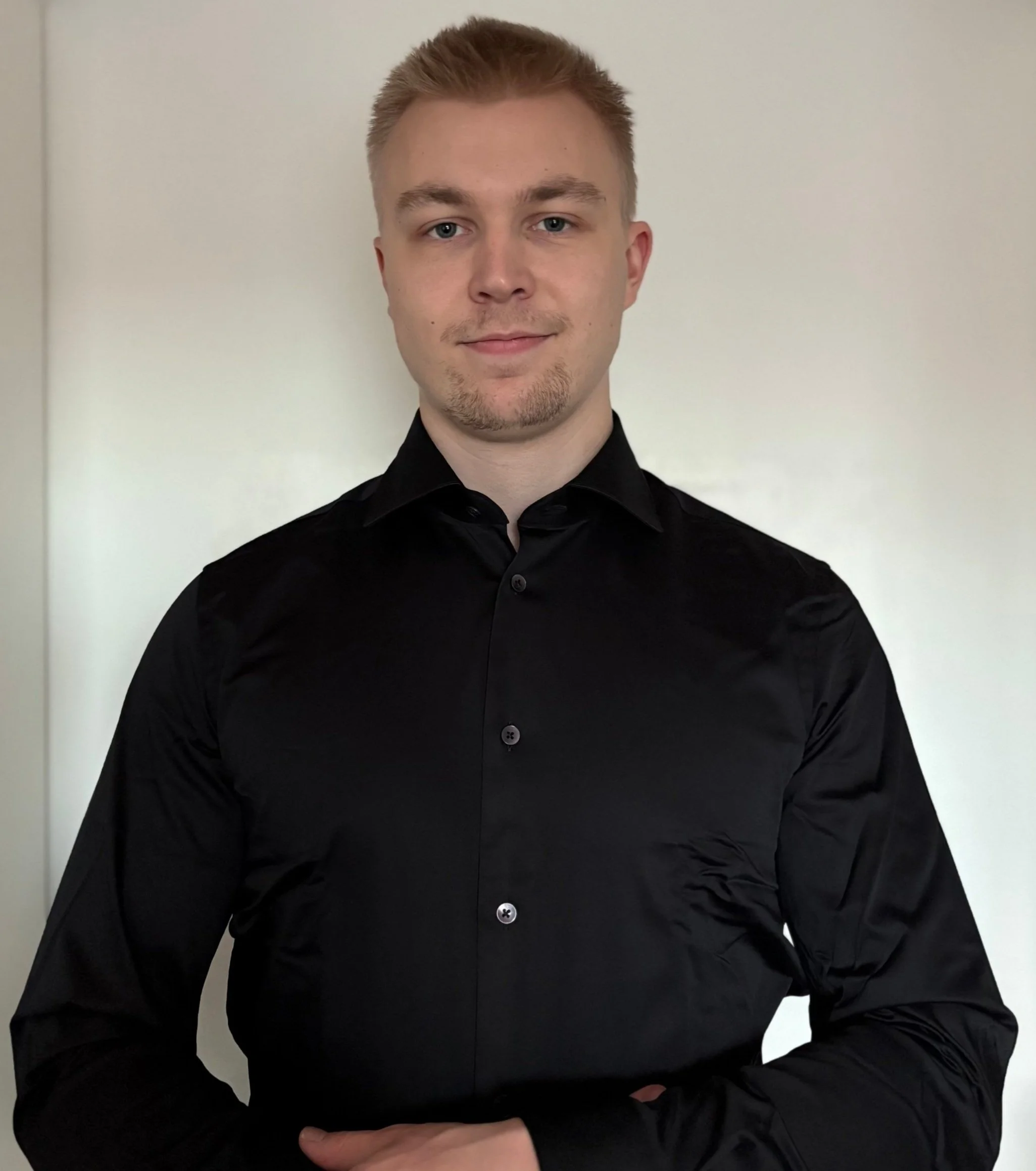 Person wearing a black dress shirt standing in front of a white background.
