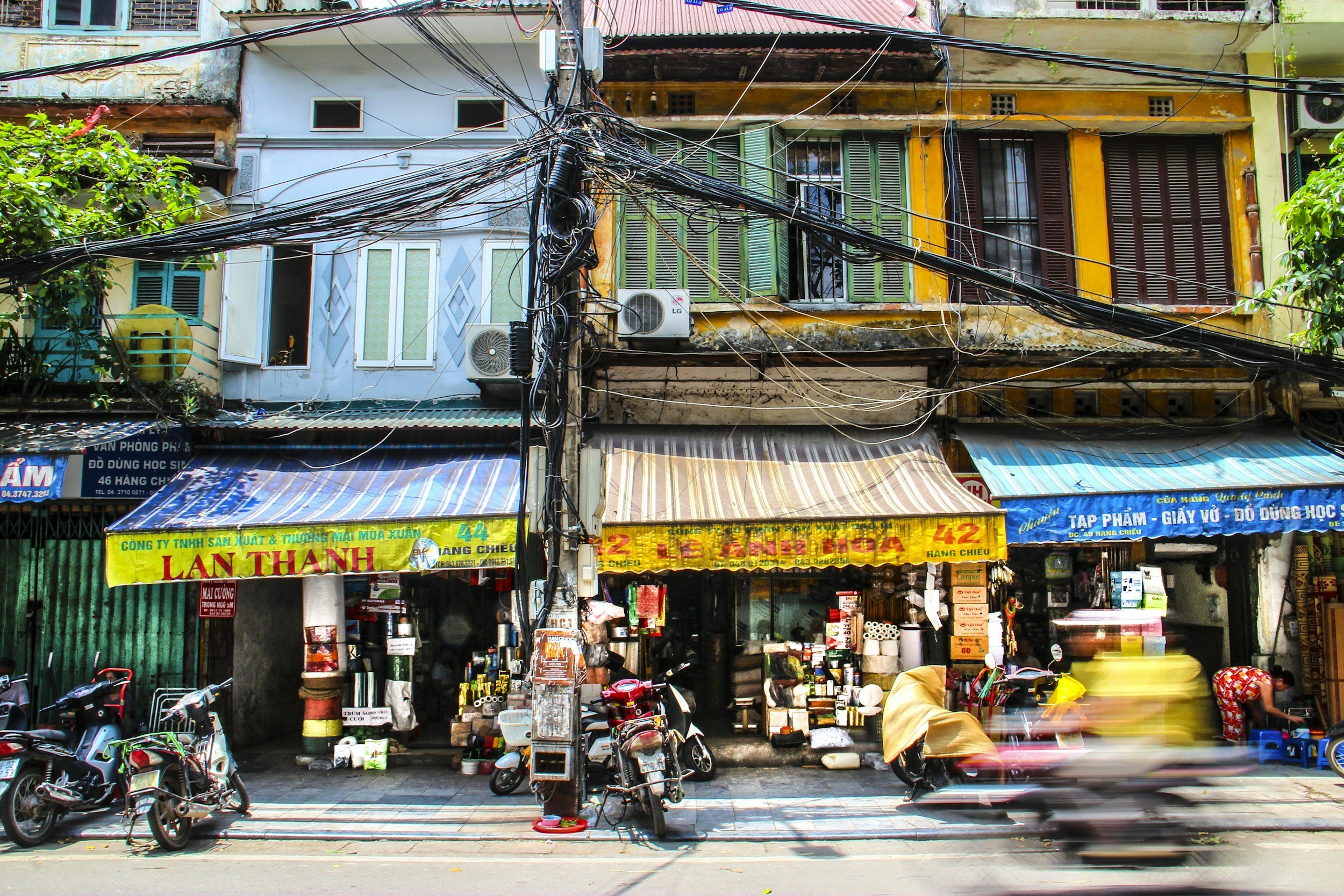 Busy Southeast Asian street with colorful shopfronts and motorbikes, the kind of neighborhood to walk before renting