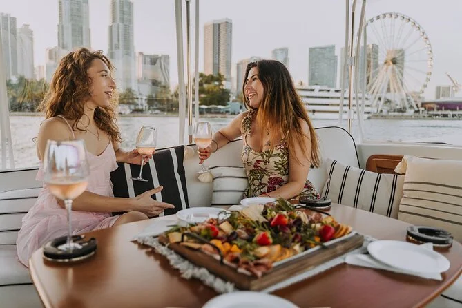 Two women enjoying wine and conversation on a river cruise with a city skyline in the background